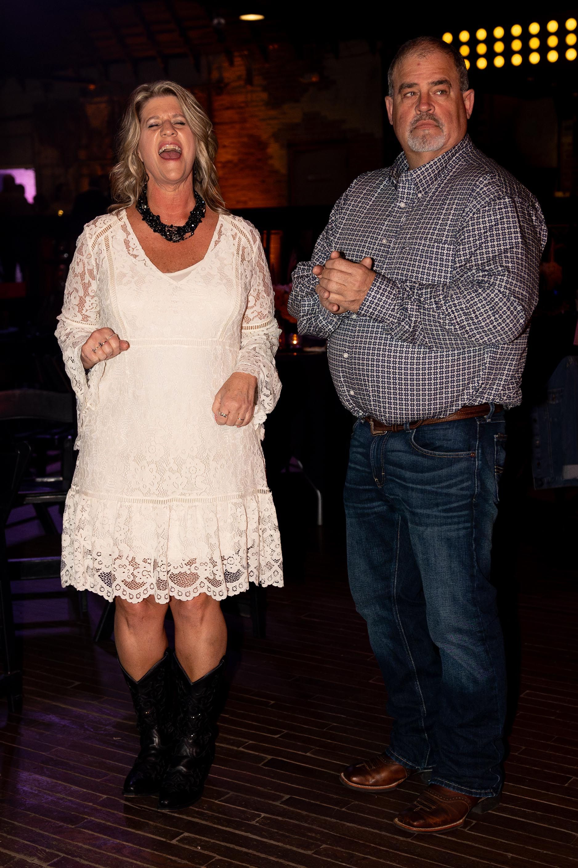 Woman in white dress and cowboy boots dancing with a man in a patterned shirt and jeans.