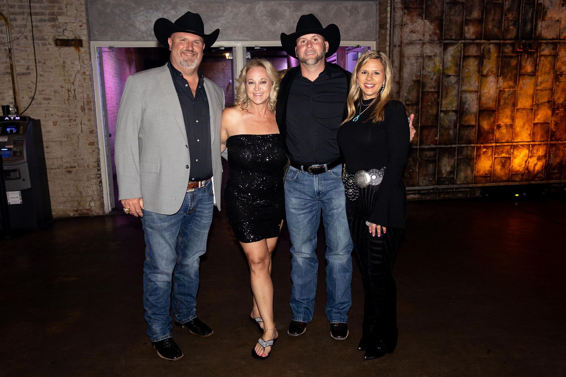 Four people in cowboy hats pose indoors. Two men, two women, in casual attire.