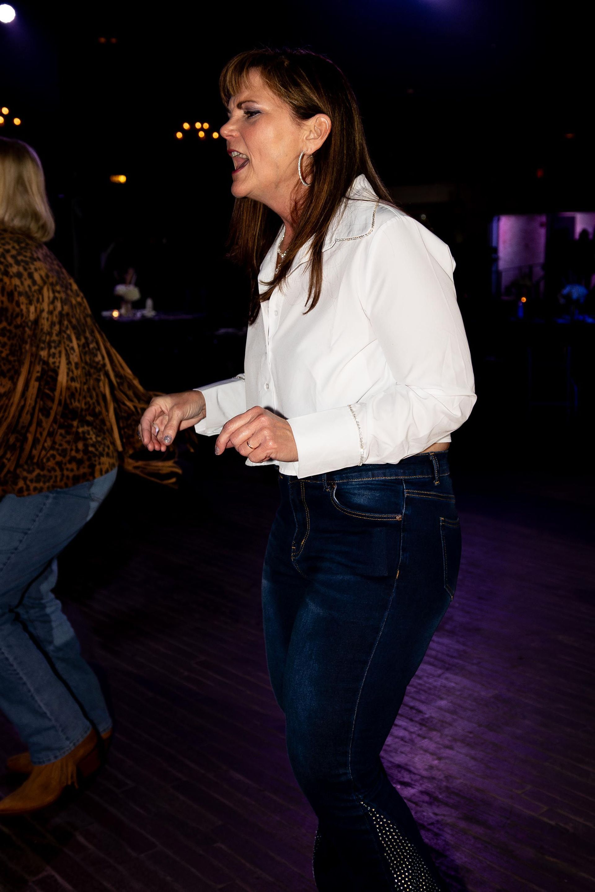 Woman in white shirt and jeans dancing on a wooden floor, with a blurred background.