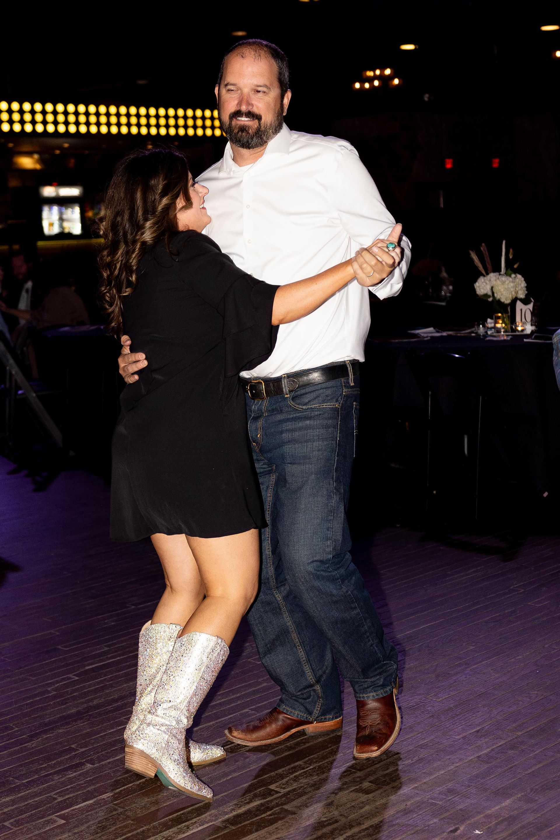 Woman in black dress and silver boots dances with a man in white shirt and jeans.