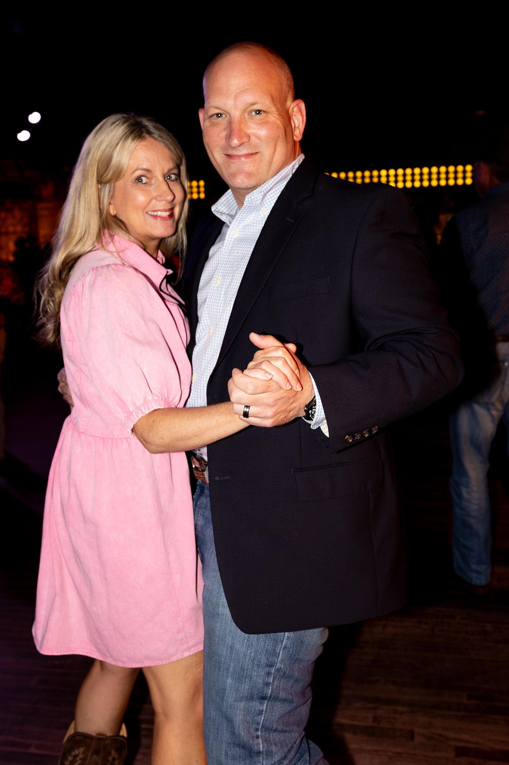 Couple dancing, woman in pink dress, man in blazer. Dance floor setting, dim lighting.