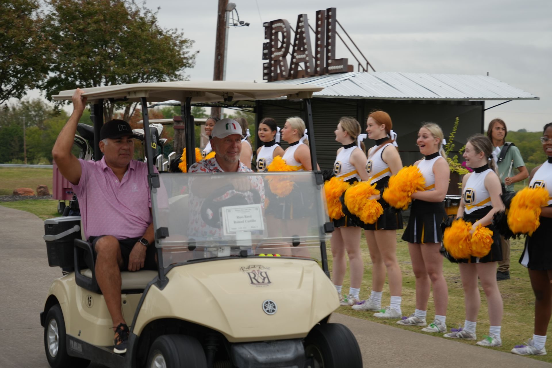 Golf cart with men, cheerleaders with yellow pom-poms, and a 