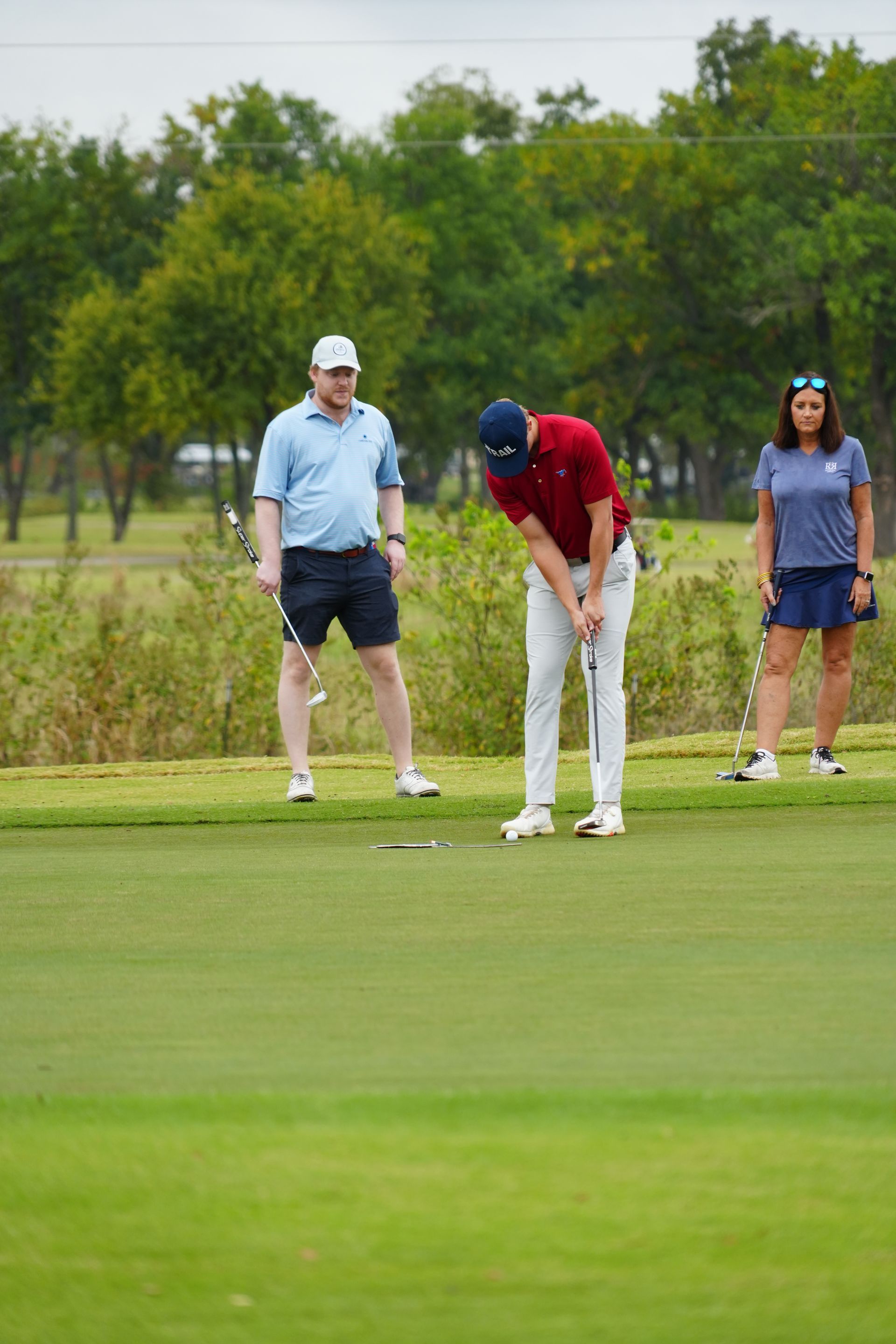 A golfer putting on a green, watched by two others in casual wear.