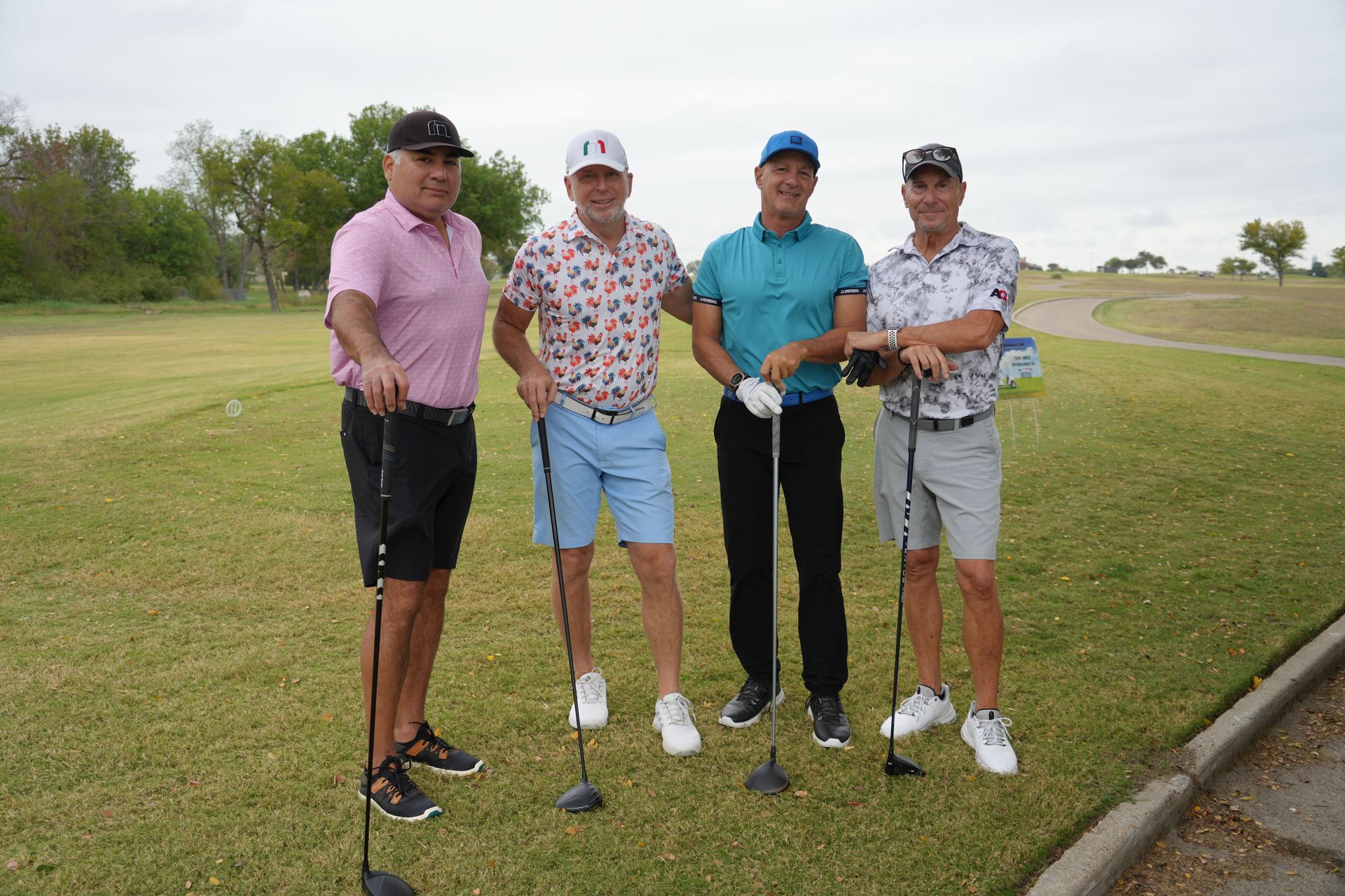 Four men on a golf course, posed with golf clubs, wearing golf attire.