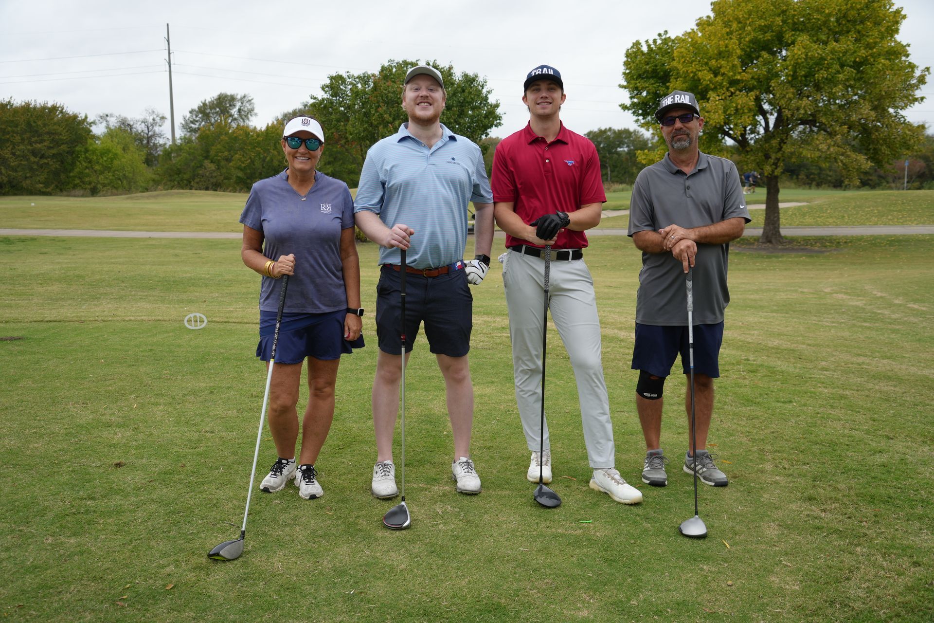 Four golfers posing on a green course, smiling, holding clubs.