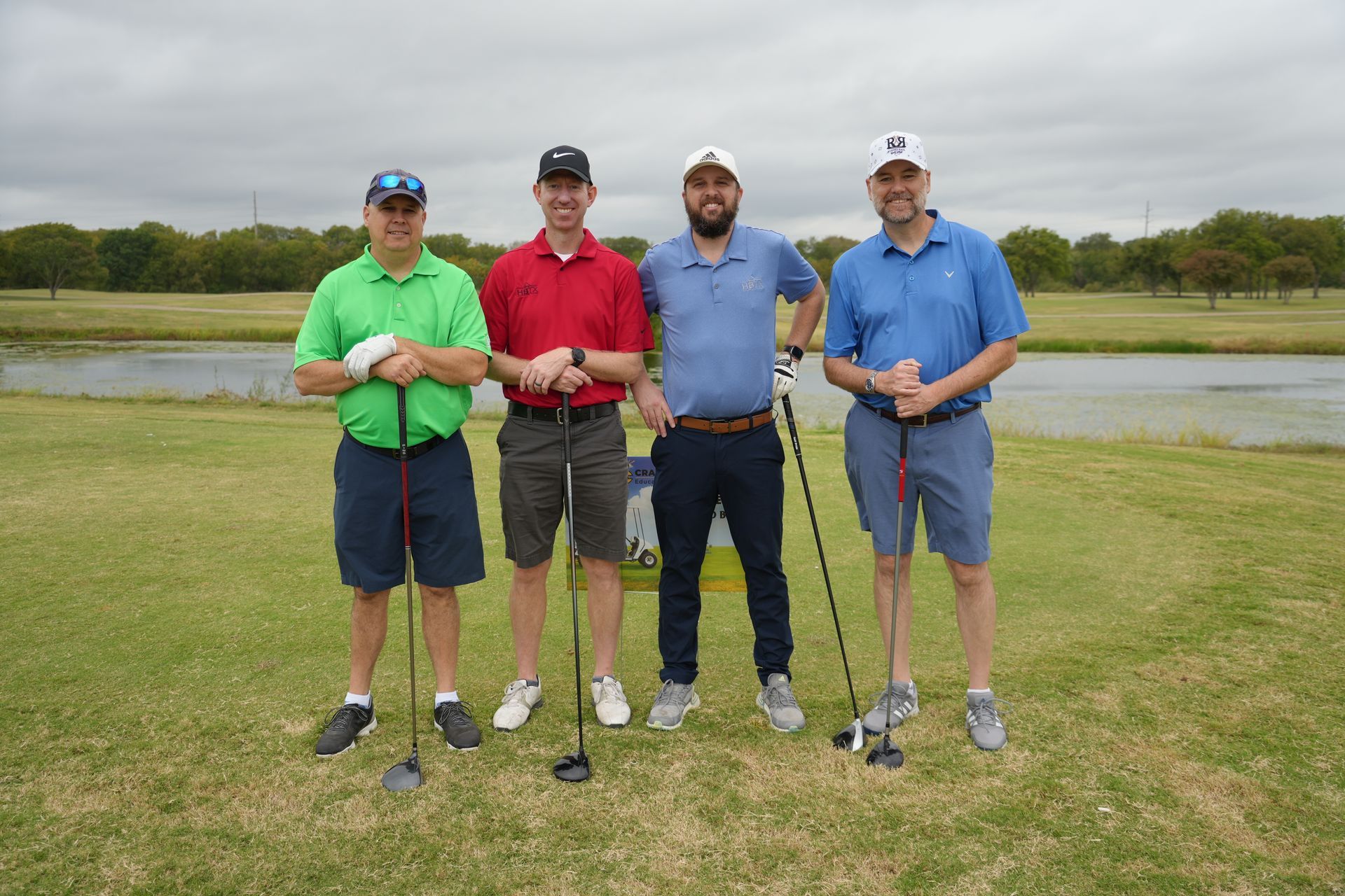 Four men in golf attire standing on a golf course, holding clubs, posing for a photo.
