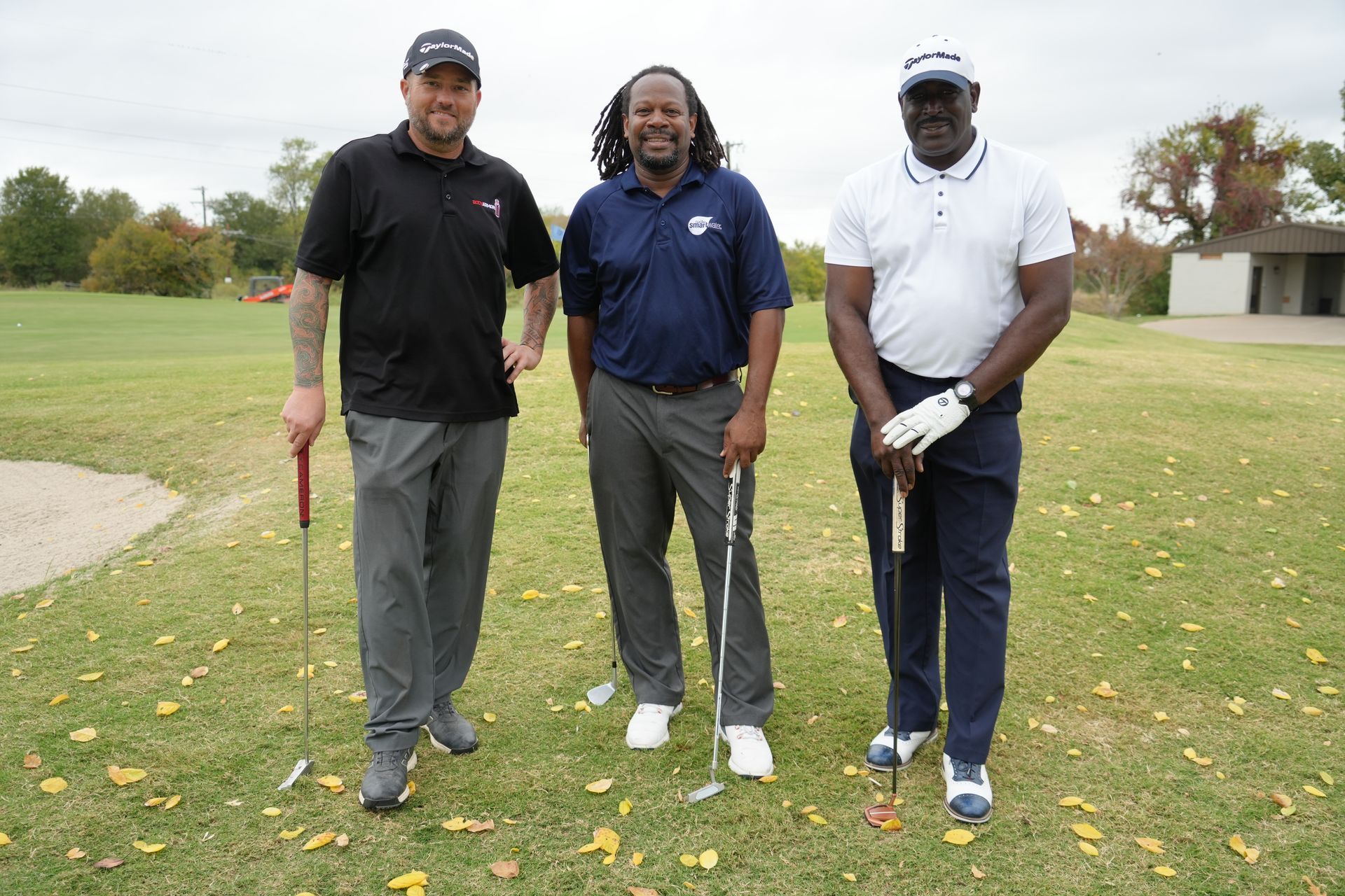 Three men standing on a golf course, holding clubs. Cloudy sky.