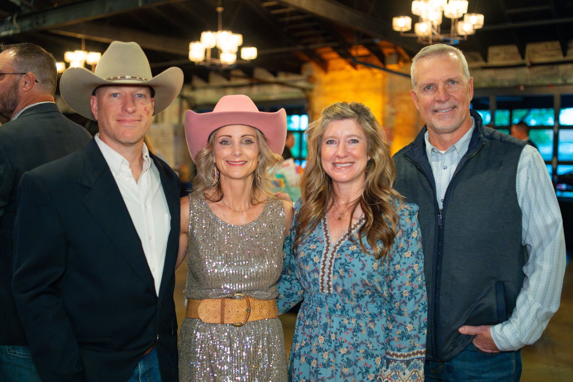 Four people posing indoors: two men, two women, all wearing cowboy hats, smiling.