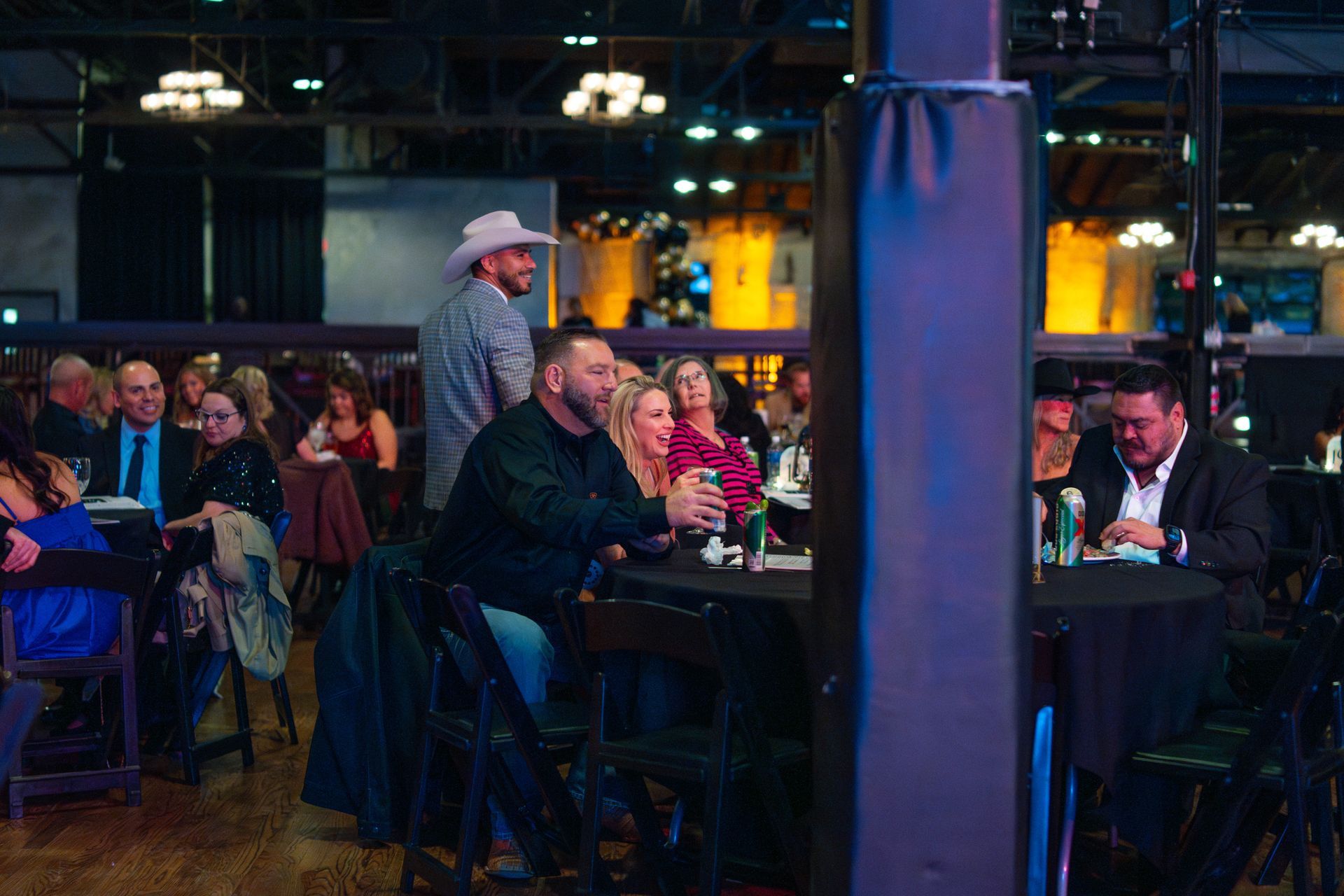 People at tables in a dimly lit venue, watching a performer on a stage.