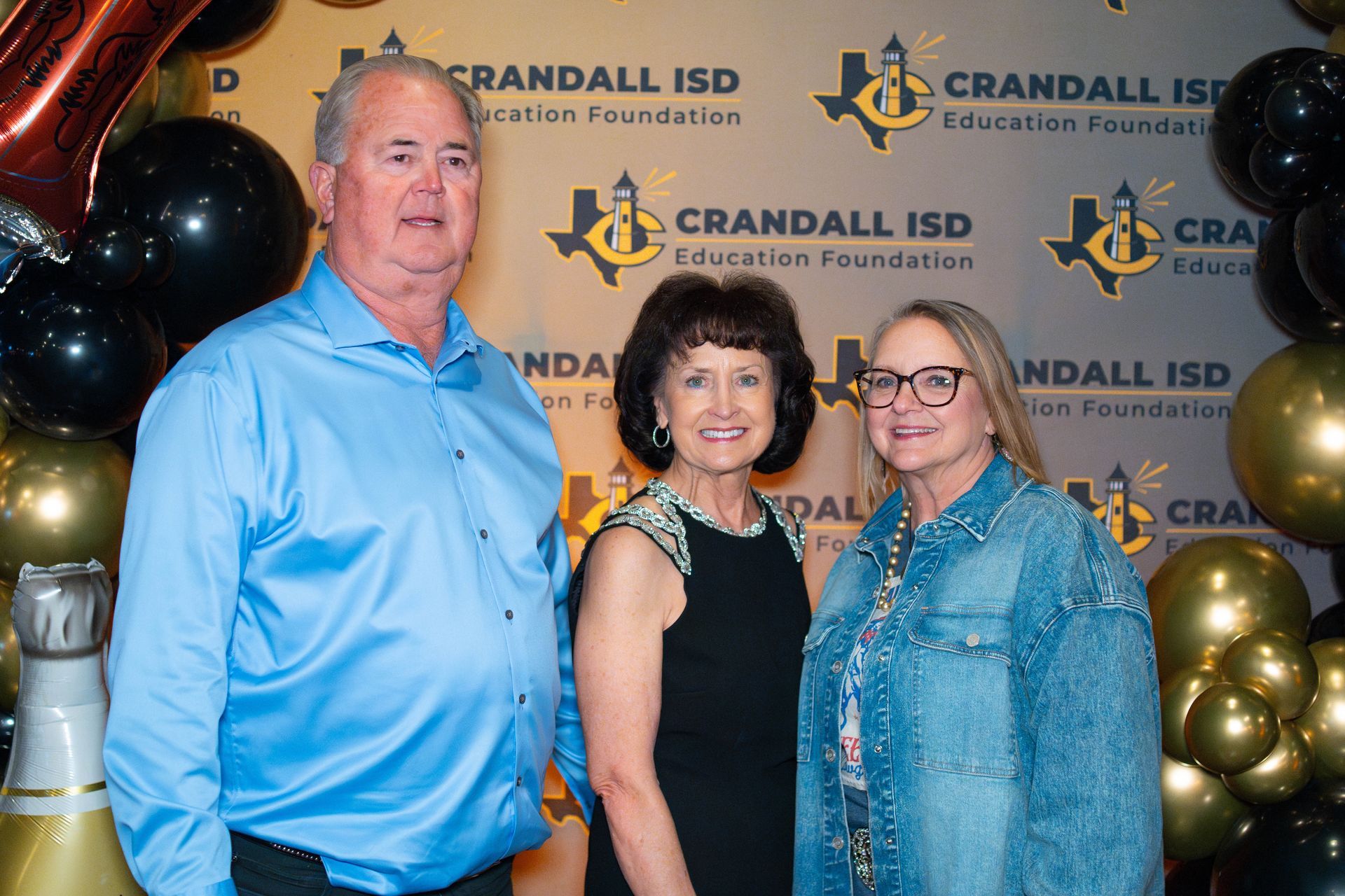 Three people pose for a photo at a Crandall ISD Education Foundation event; backdrop with balloons.