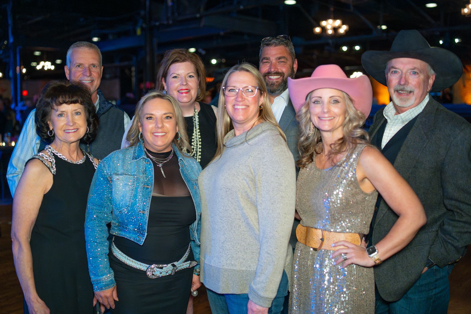 Group of eight people, some in western attire, smiling in a venue with chandeliers.