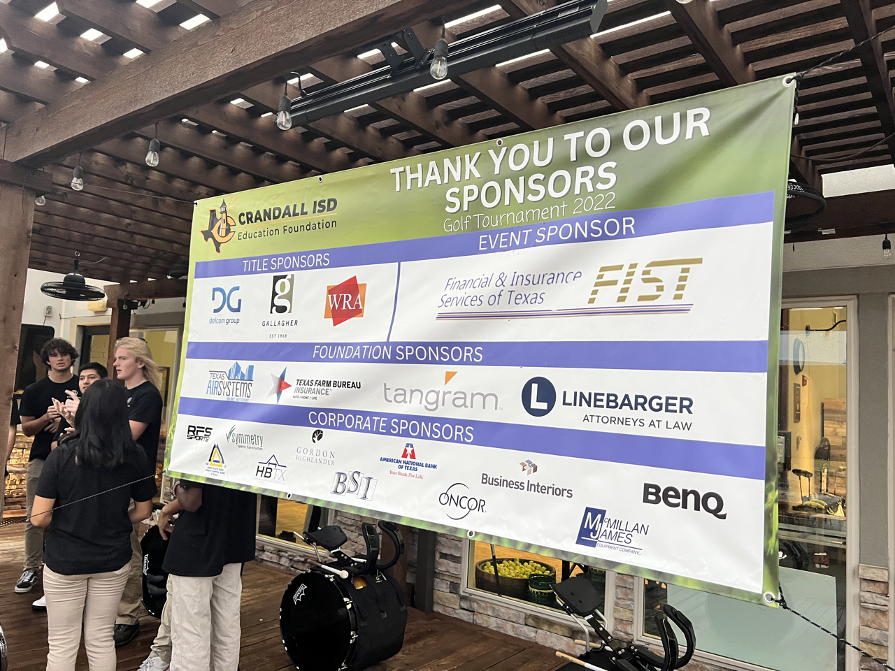 Banner thanking sponsors at an event, with people standing near it.