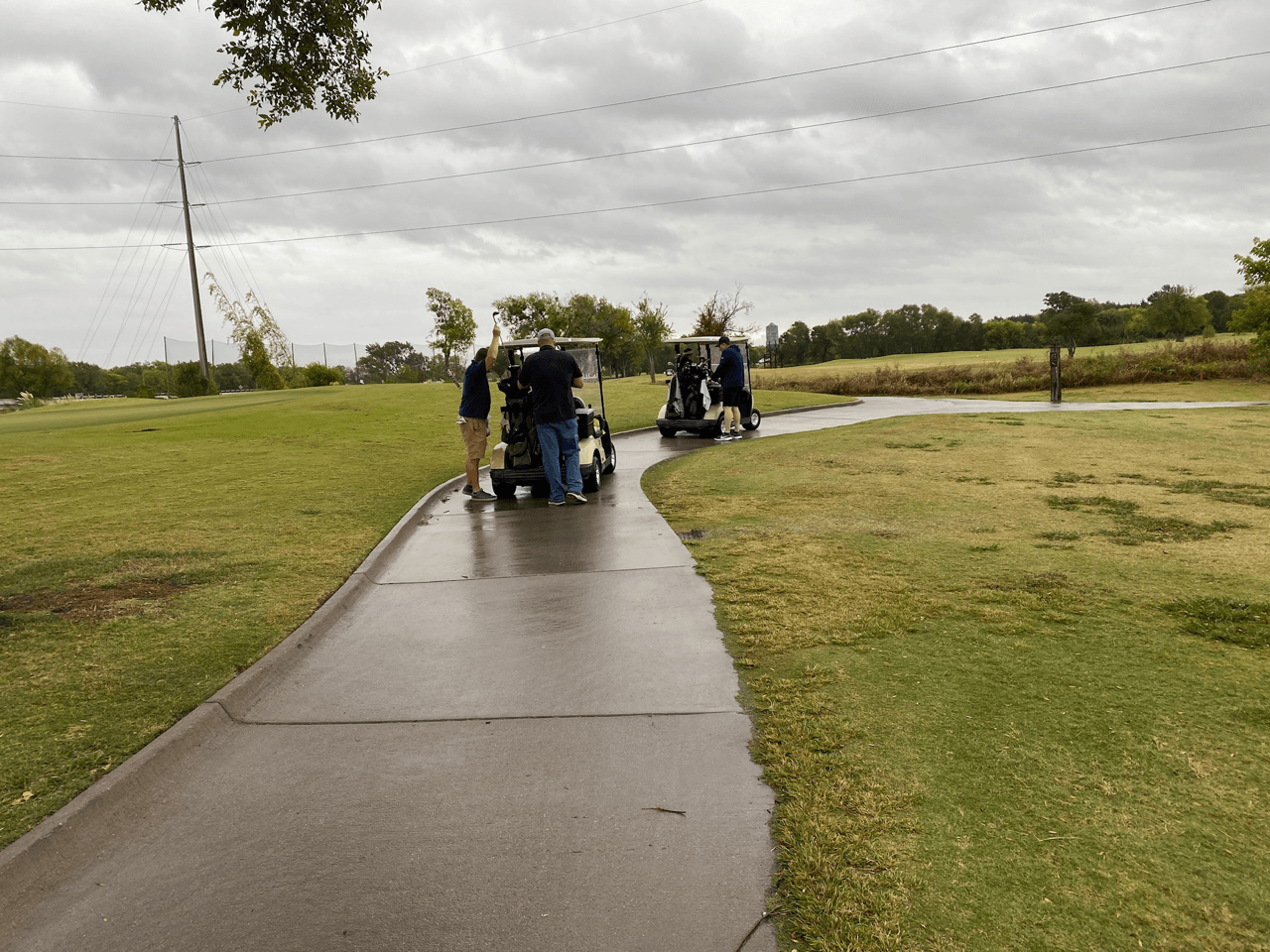 Two golf carts on a wet path, golfers nearby, overcast sky.
