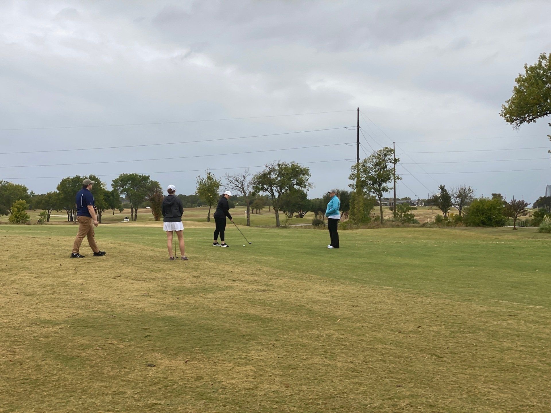 Four people playing golf on a green field under a cloudy sky.