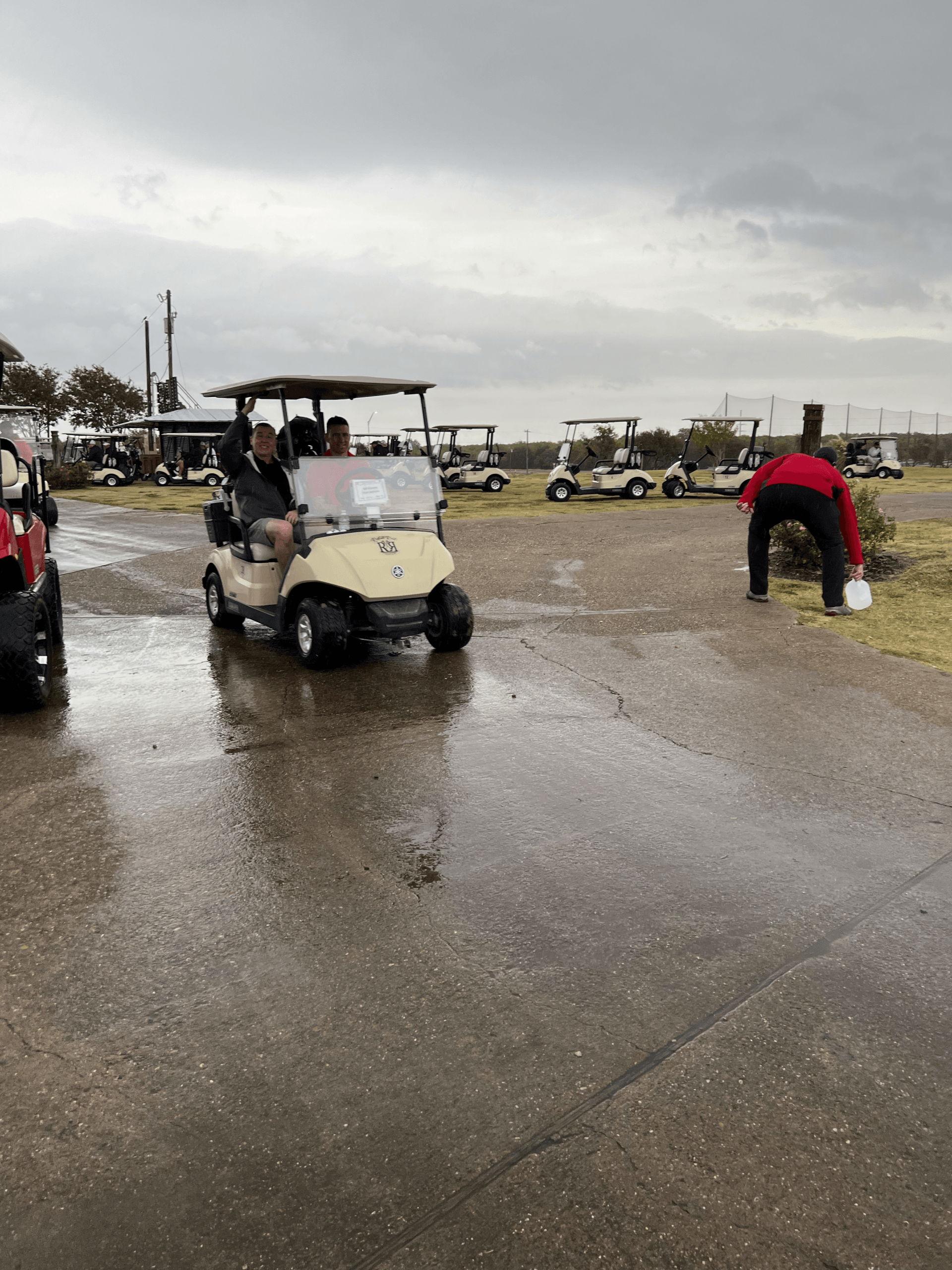 Golf carts on a wet, gray day. A person is near the cart. Other carts and trees are in the background.