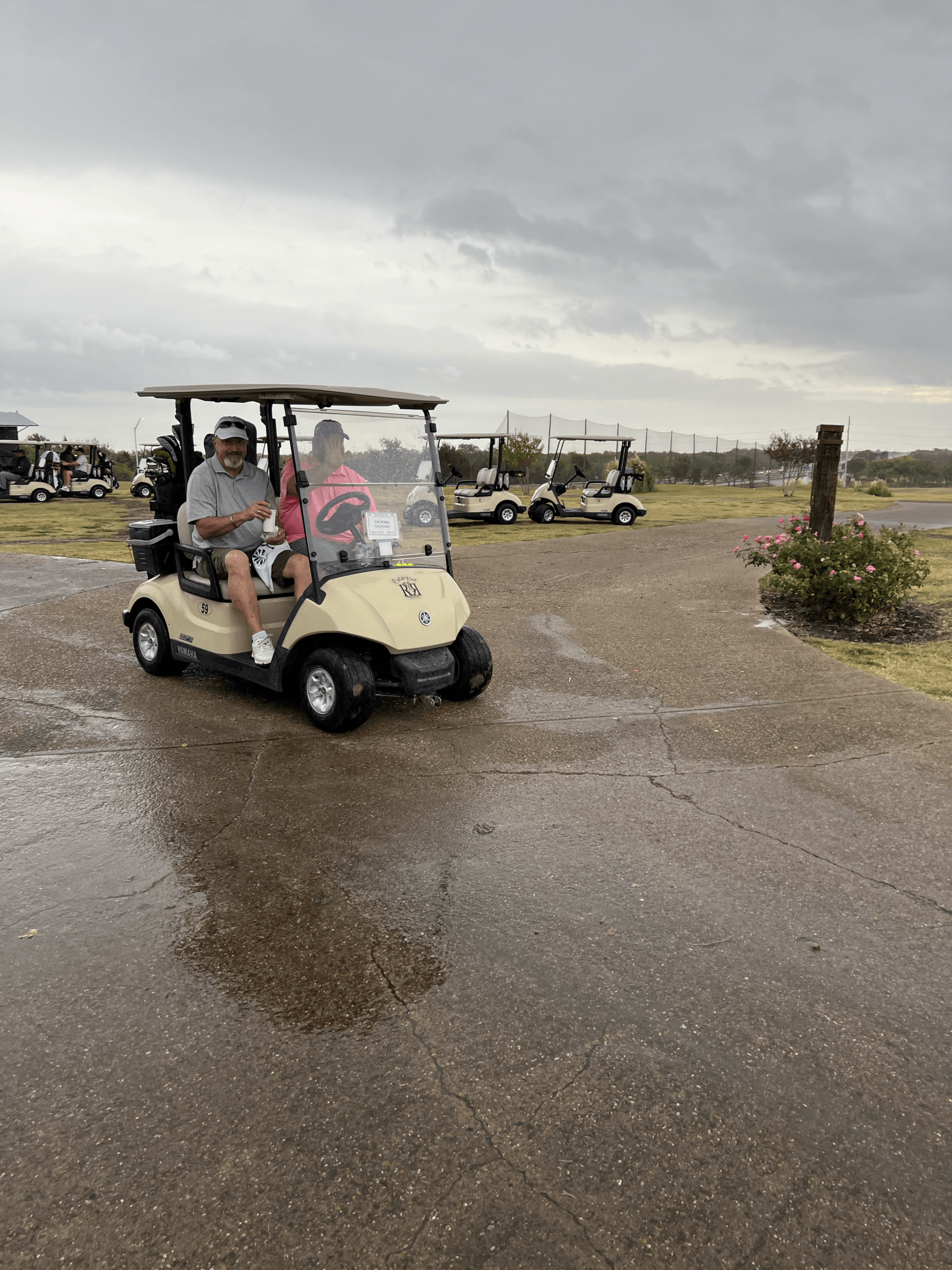 A golf cart with two people driving on a wet surface in a cloudy environment.