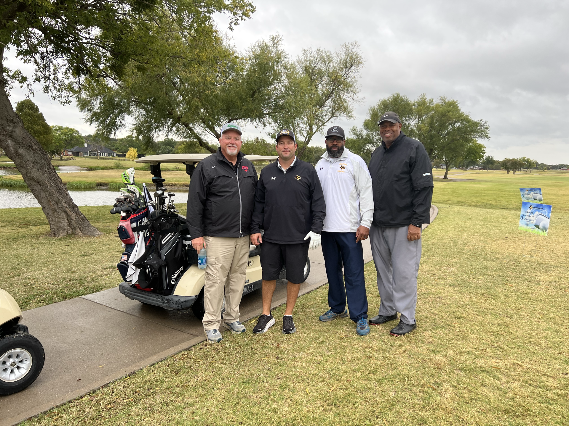 Four men pose for a photo next to a golf cart on a golf course.