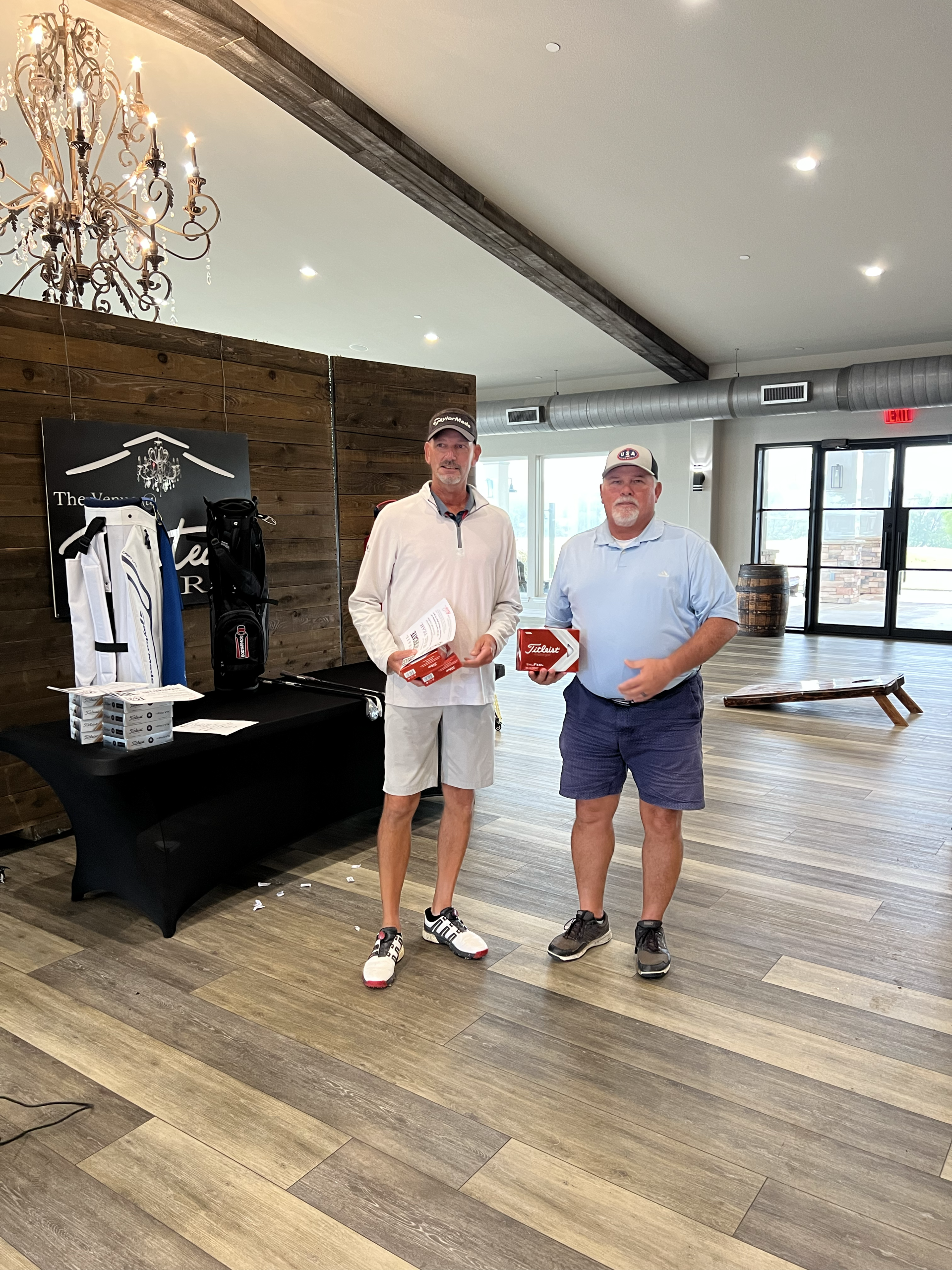 Two men holding awards inside a building with a rustic decor and a chandelier.