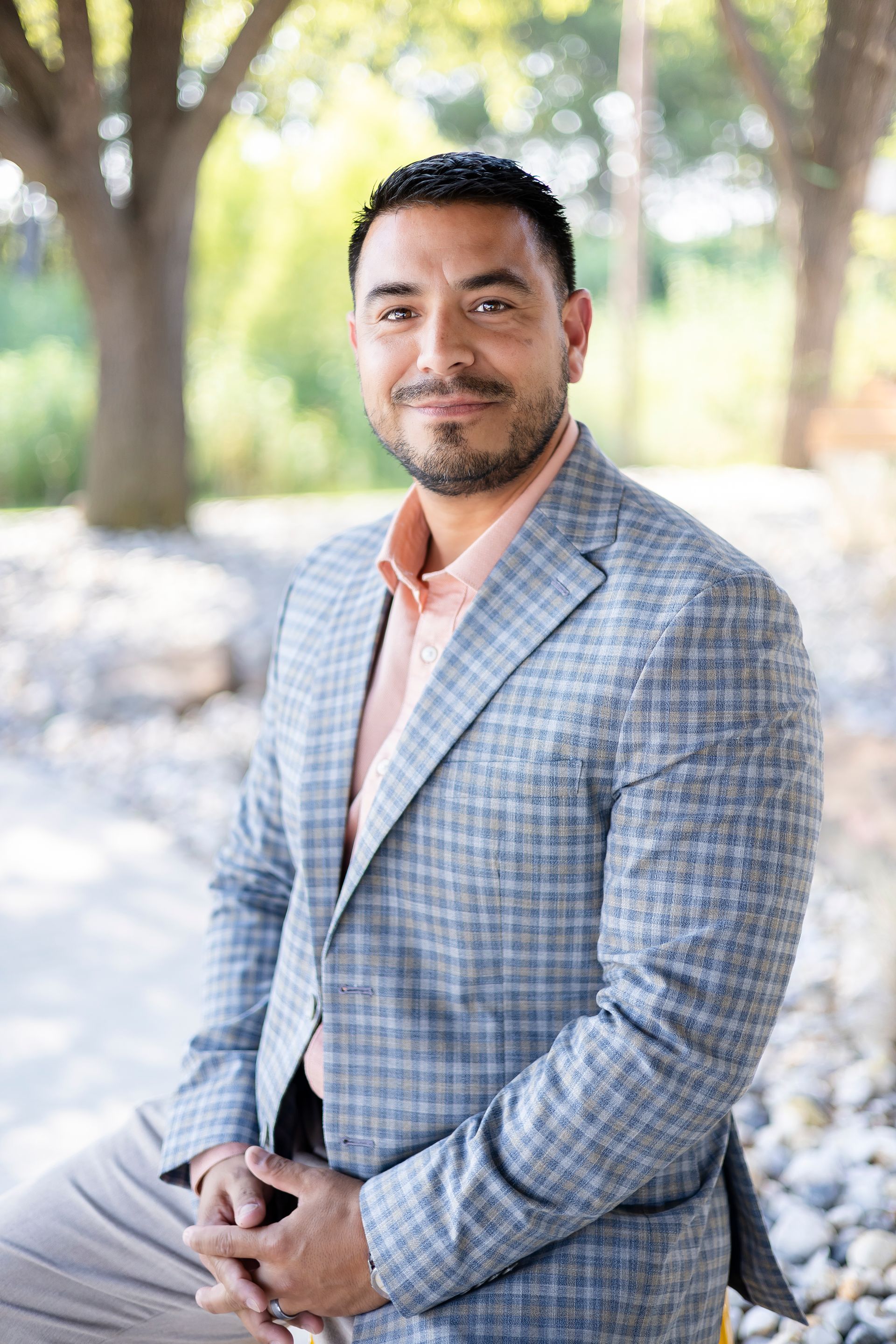 Man in blazer smiles outdoors.