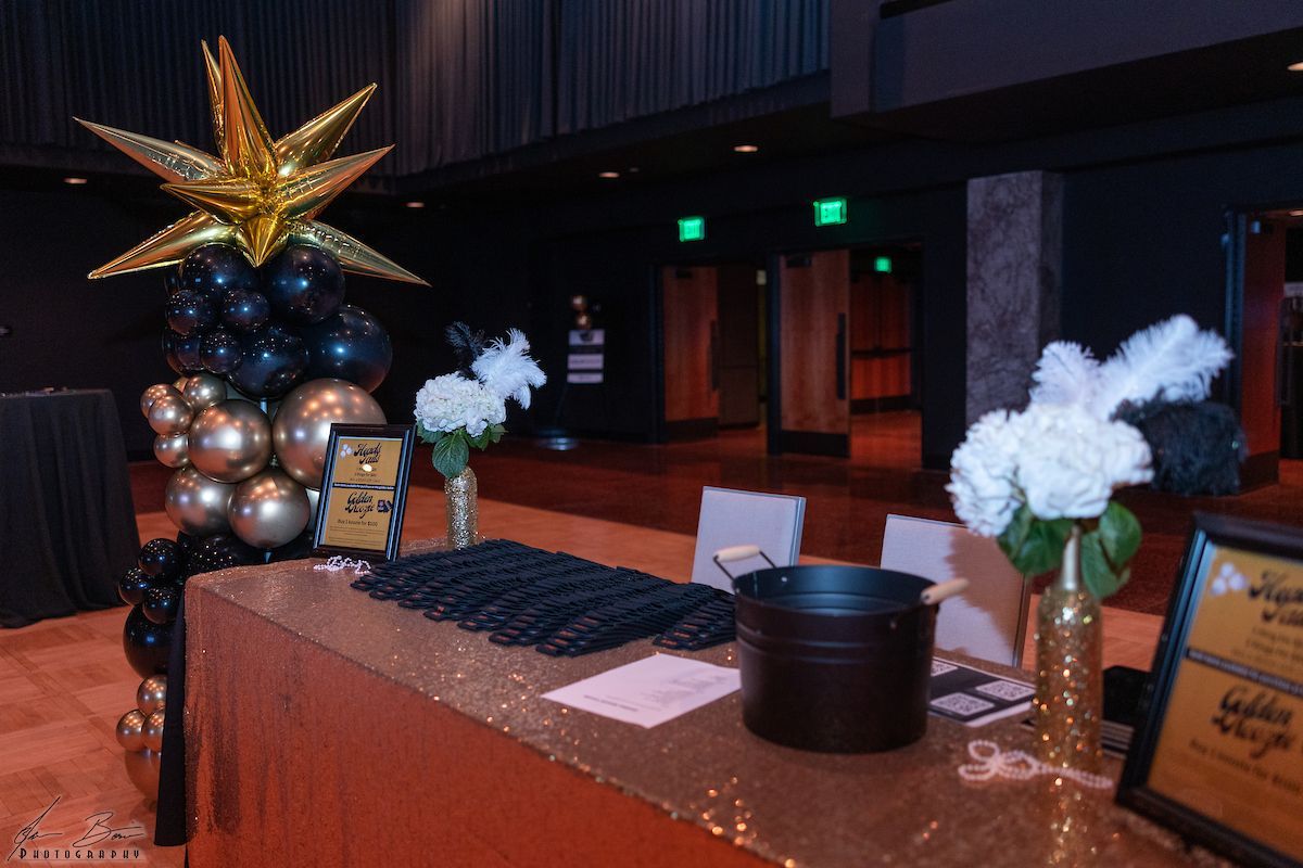 Reception table with gold sequin tablecloth, black and gold balloons, floral arrangements.