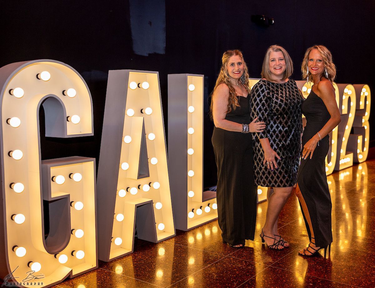 Three women pose by large, lighted 