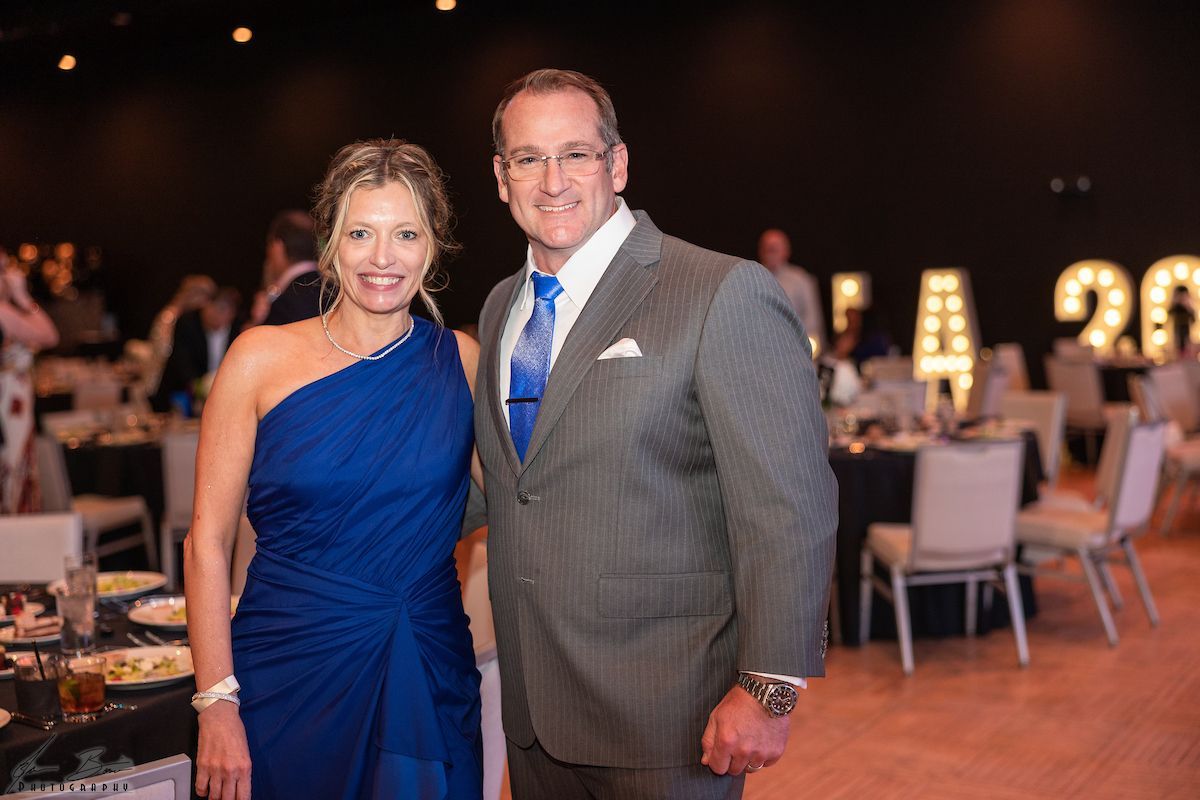 A woman in a blue gown and a man in a suit pose at an event with lit-up 