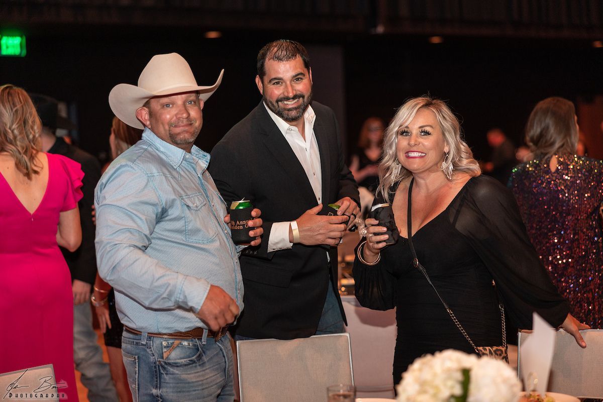 Three people smiling at an event, one in a cowboy hat, others holding drinks.