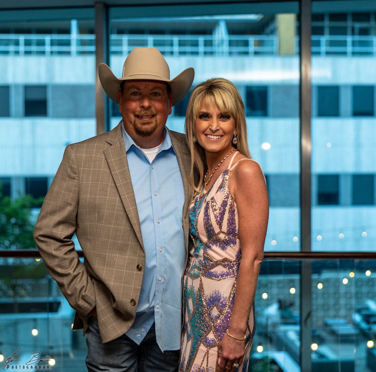 Man in cowboy hat and woman in gown pose together by a window.