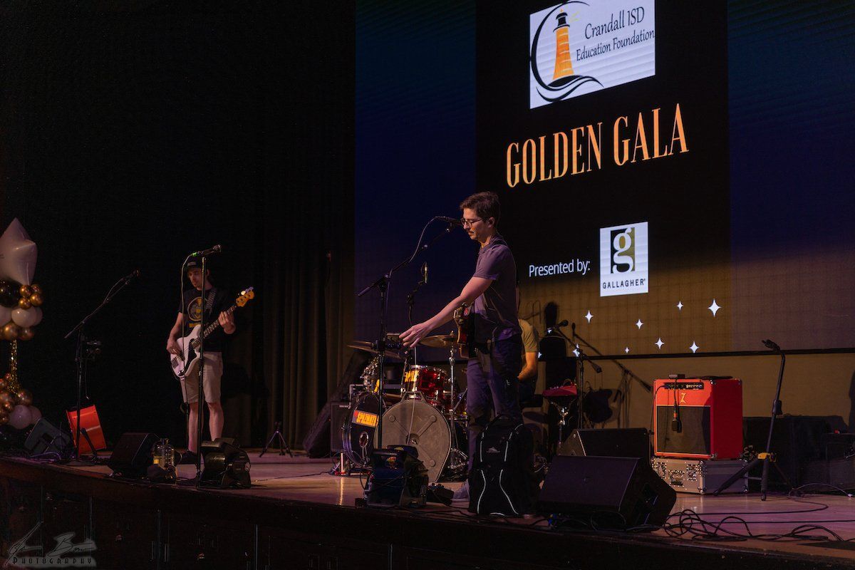 Band playing on stage at the Golden Gala. Musicians with instruments, lights and a banner.