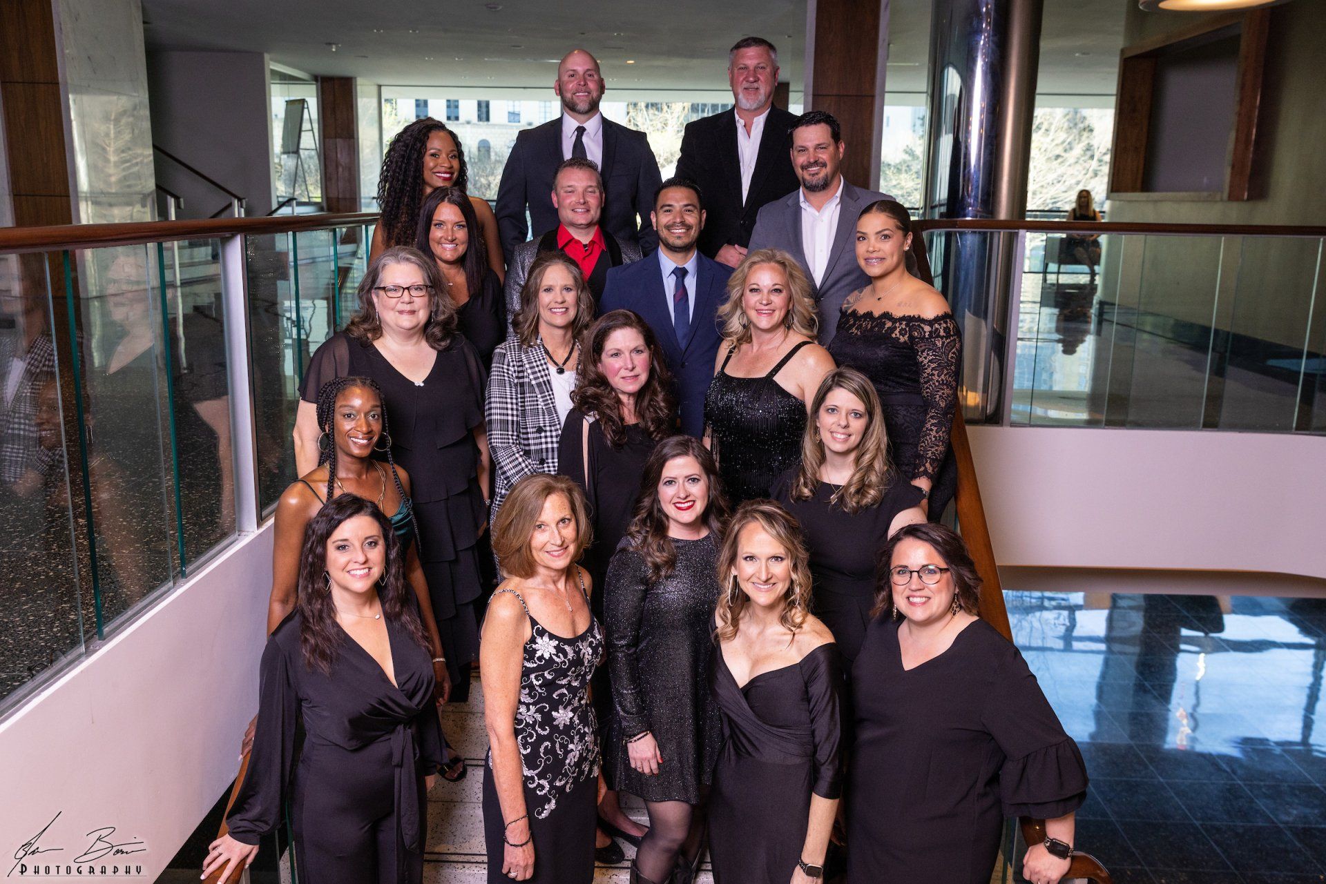 Group photo of people in formal attire on a staircase with a modern interior setting.
