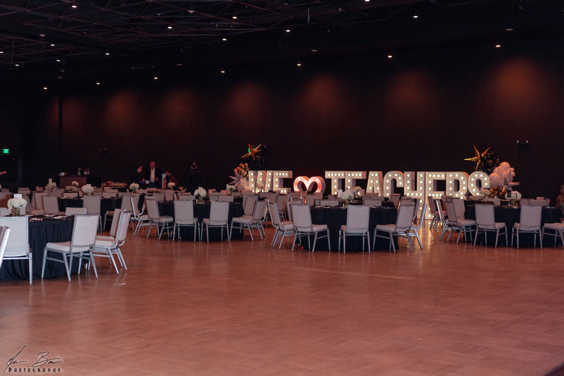 Ballroom decorated for an event. Tables are set with black linens. Illuminated letters spell 