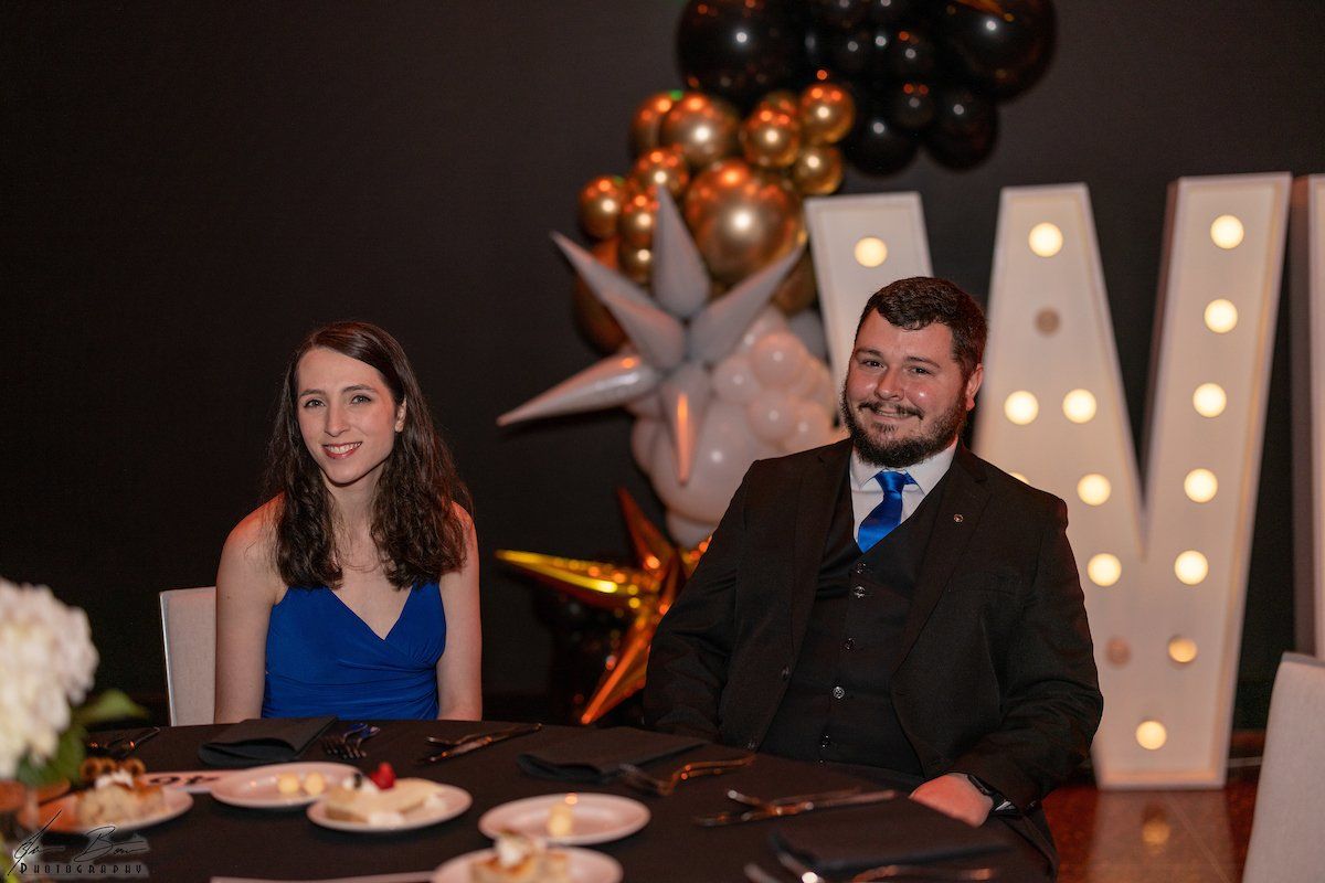 A woman in a blue dress and a man in a suit at a table in a decorated room with balloons.