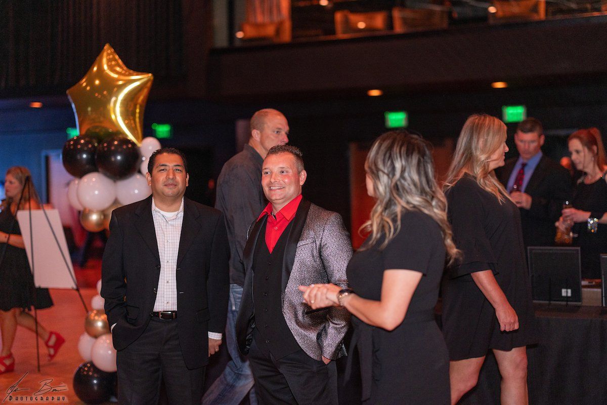 People at an event, dressed in business attire, near balloons and tables.
