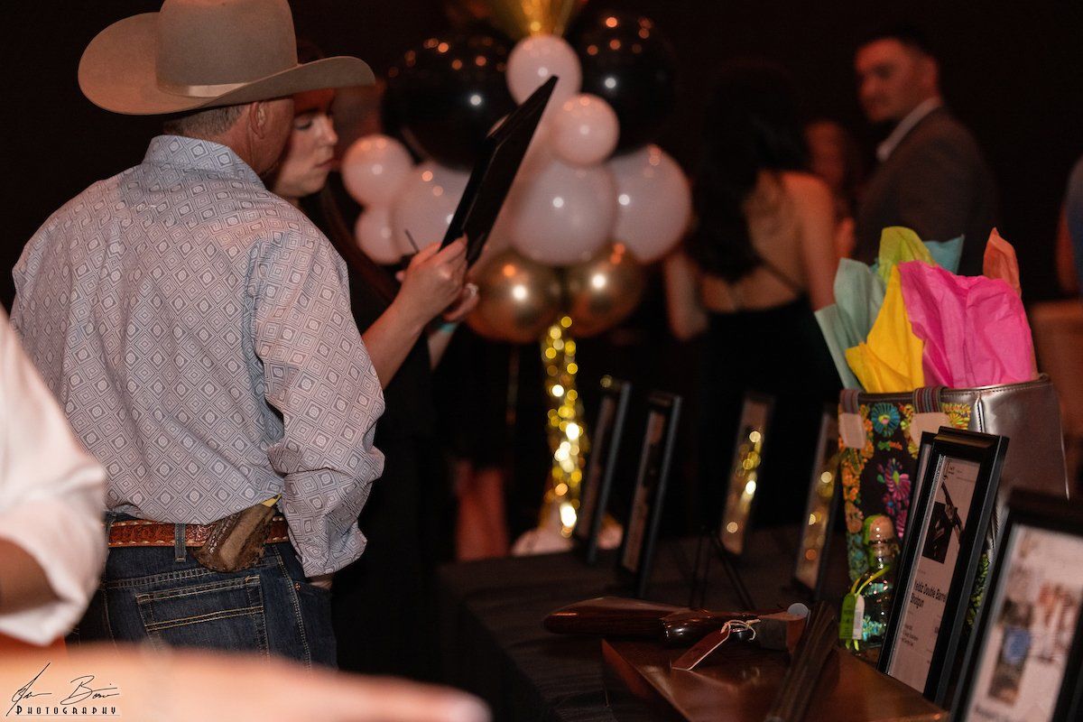 Man in cowboy hat looks at display at event. Table has framed items, balloons, and colorful decorations.