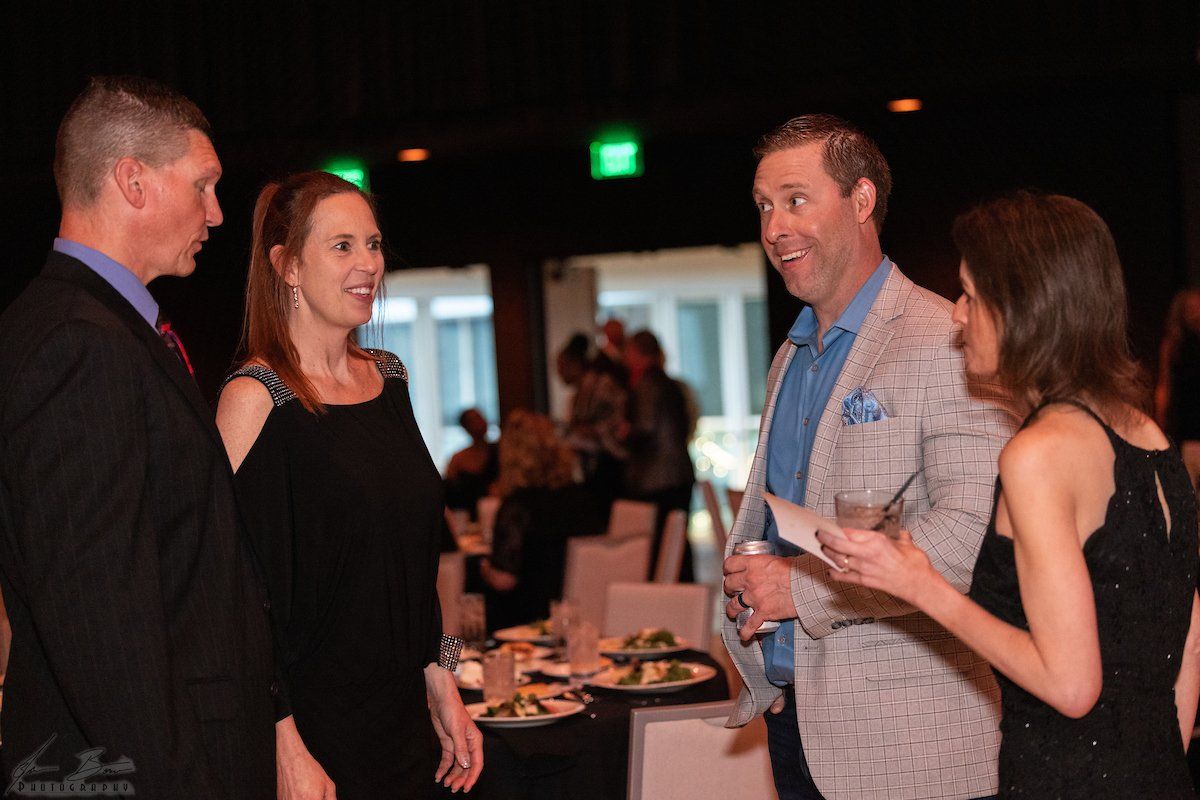 Four people, two men and two women, converse at a formal indoor event.