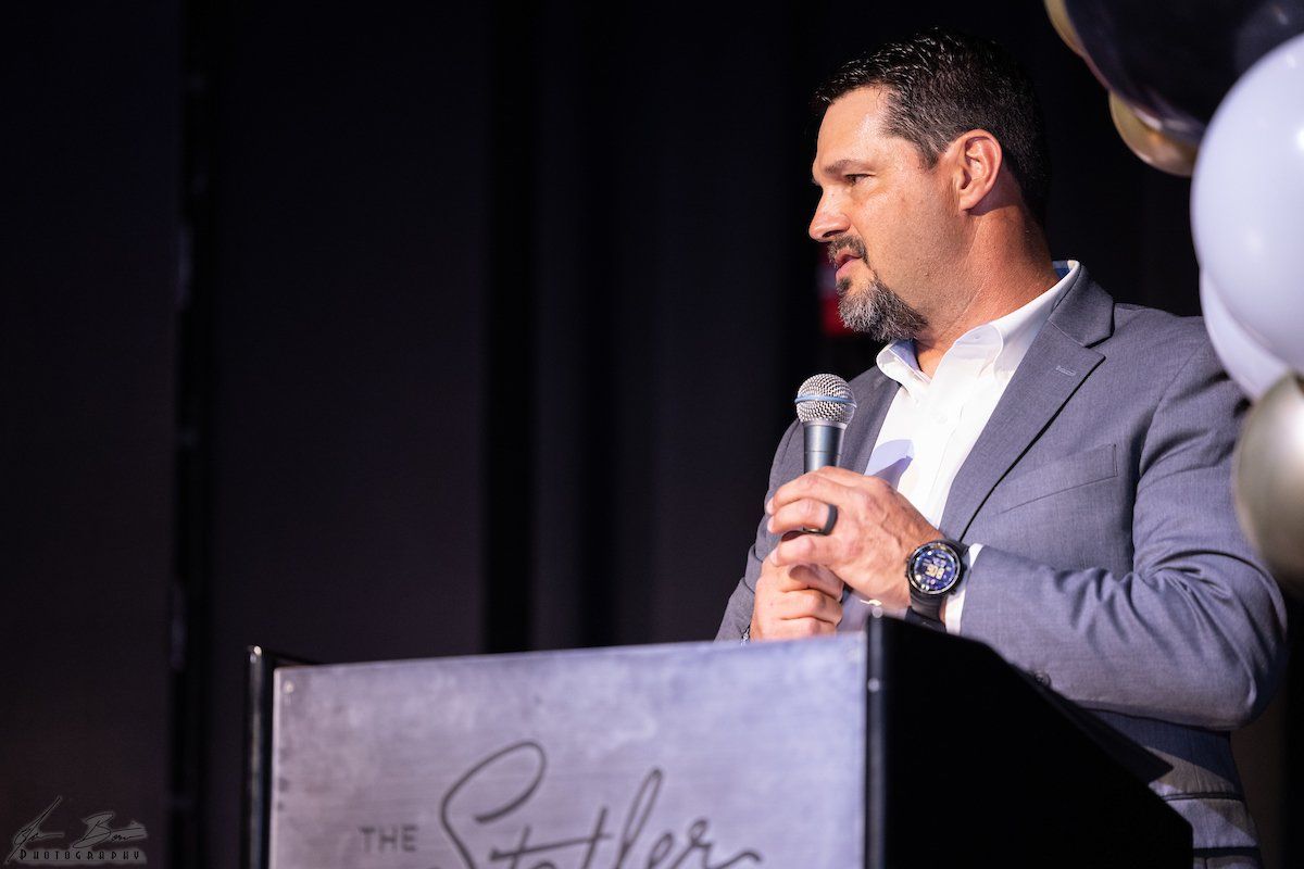 Man in gray suit speaks at podium with 