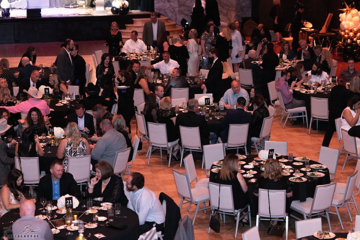 People seated at tables in a large ballroom, attending an event with food and decorations.