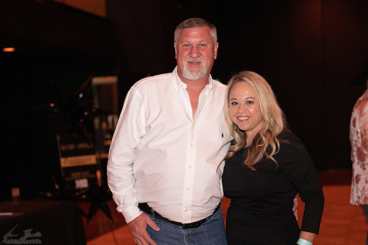 Man in white shirt and woman in black dress pose together at an event.
