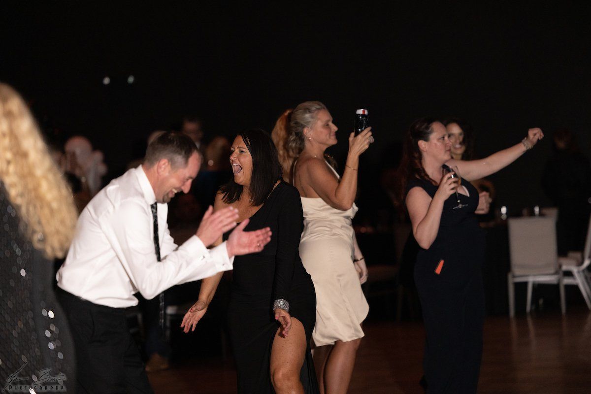People dancing and singing at an event; woman in a strapless dress holds a microphone.