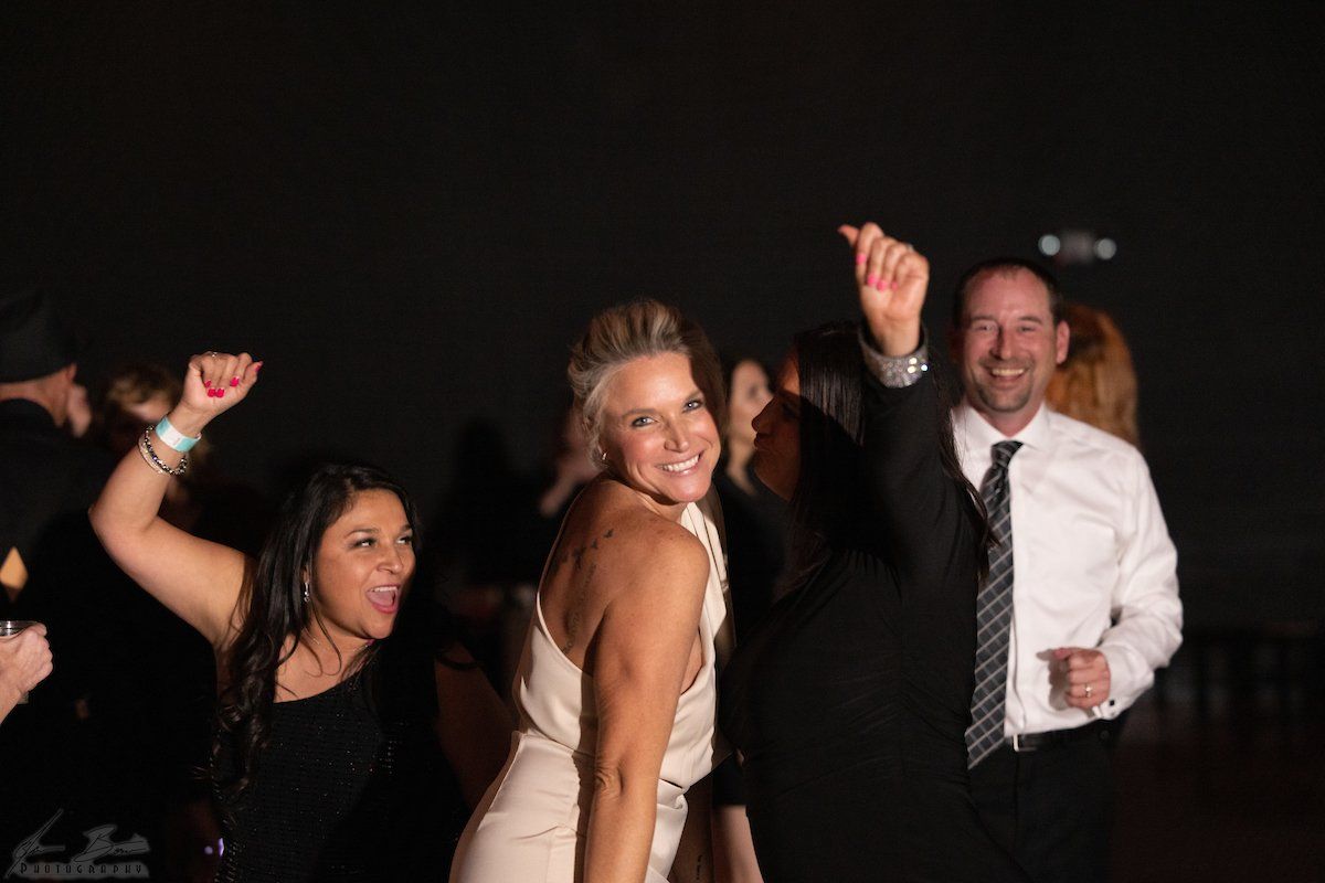People dancing joyfully at a party, smiling, some with arms raised. Dark background.