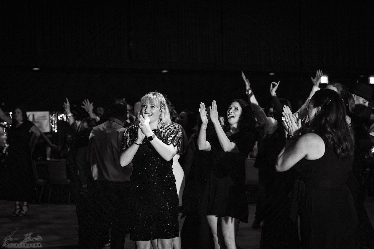 People in a dark room clap their hands and raise arms in celebration. Black and white photo.