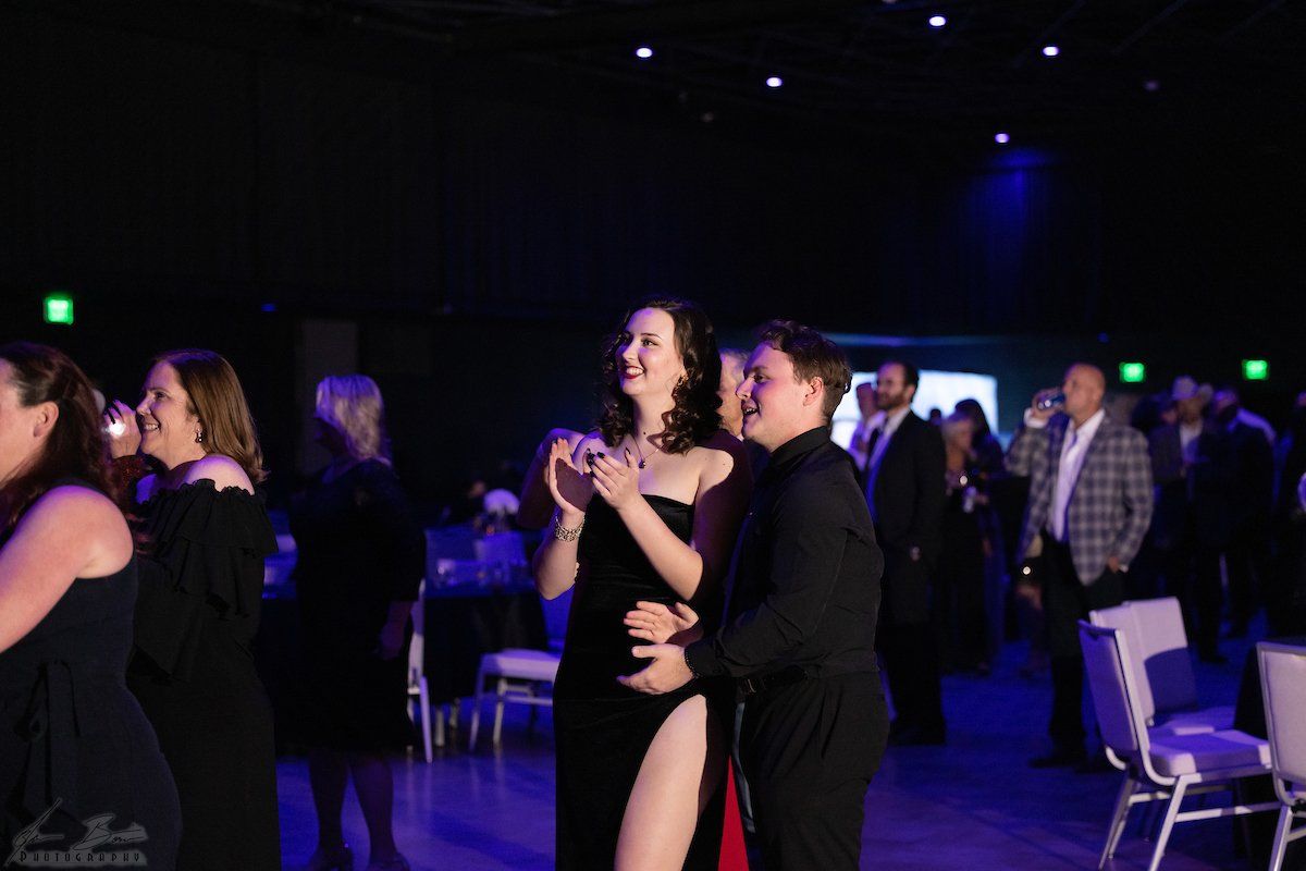 People at a formal event. A woman in a black dress laughs with a man. Blue lighting fills the room.