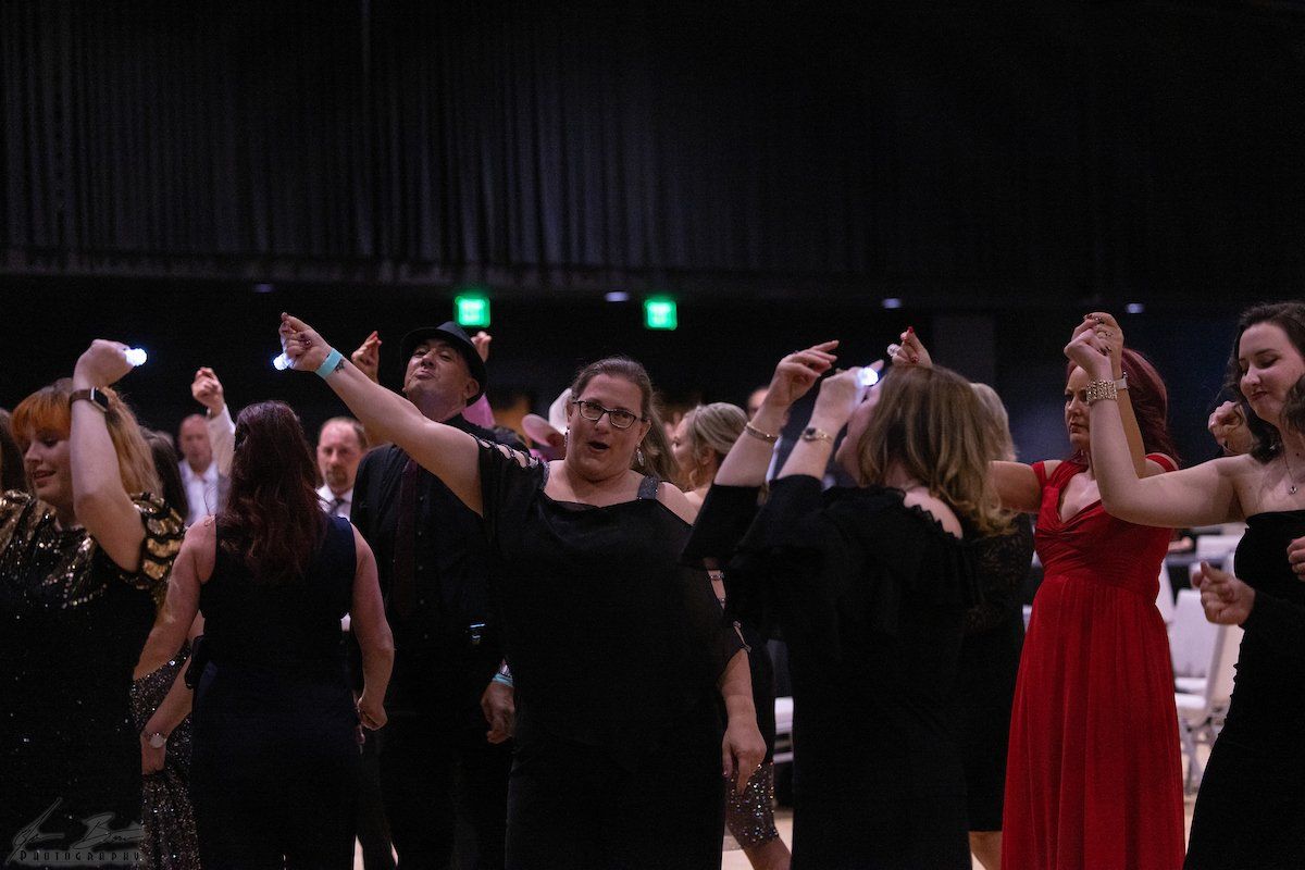 People dancing in a ballroom, holding hands and raising arms. Mostly women in black dresses.
