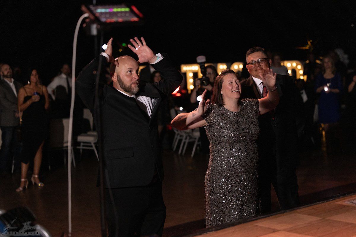 A man in a tux dances with a woman in a sparkly dress as a photographer holds a light.