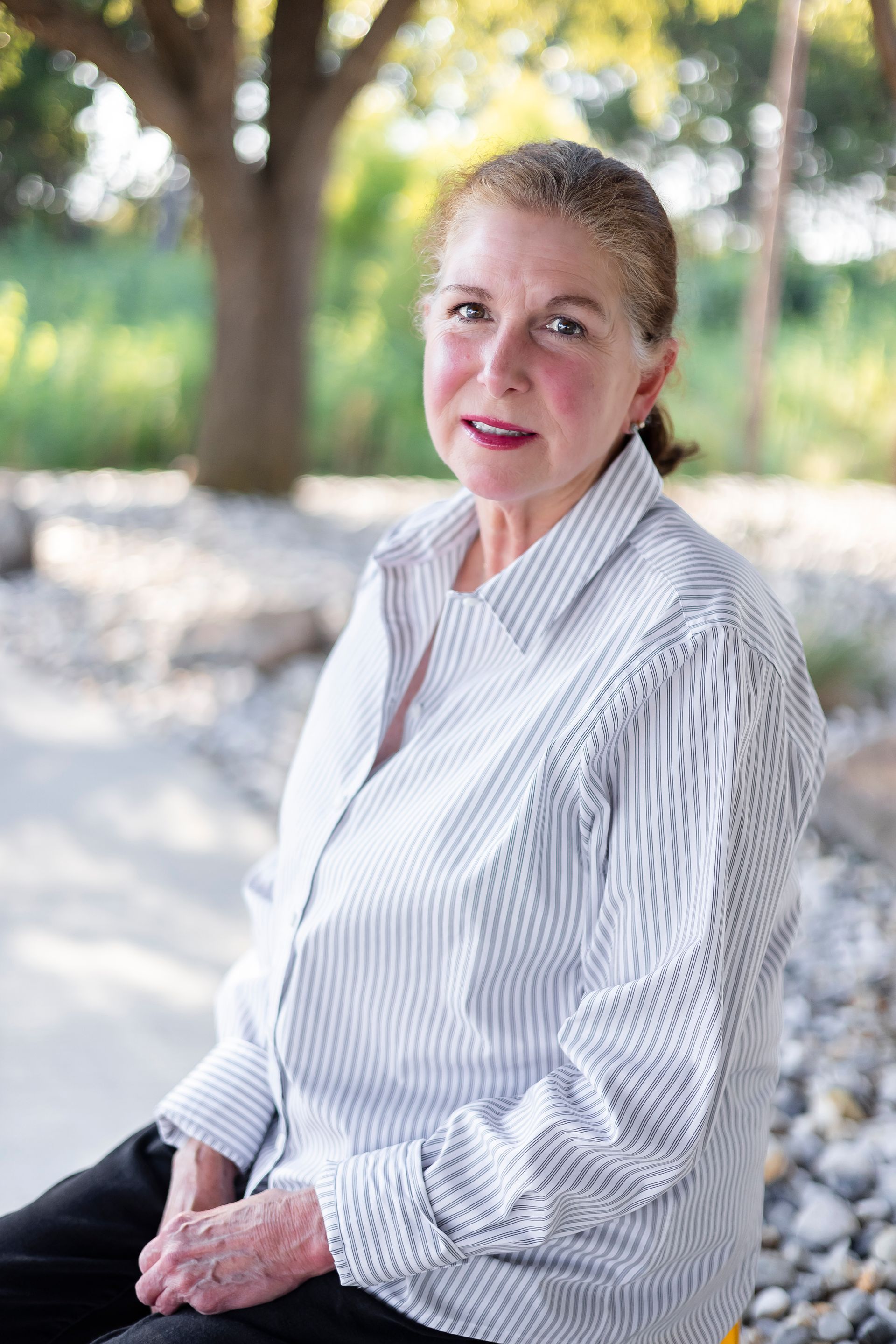 Woman with light skin smiles outdoors, wearing a striped shirt.
