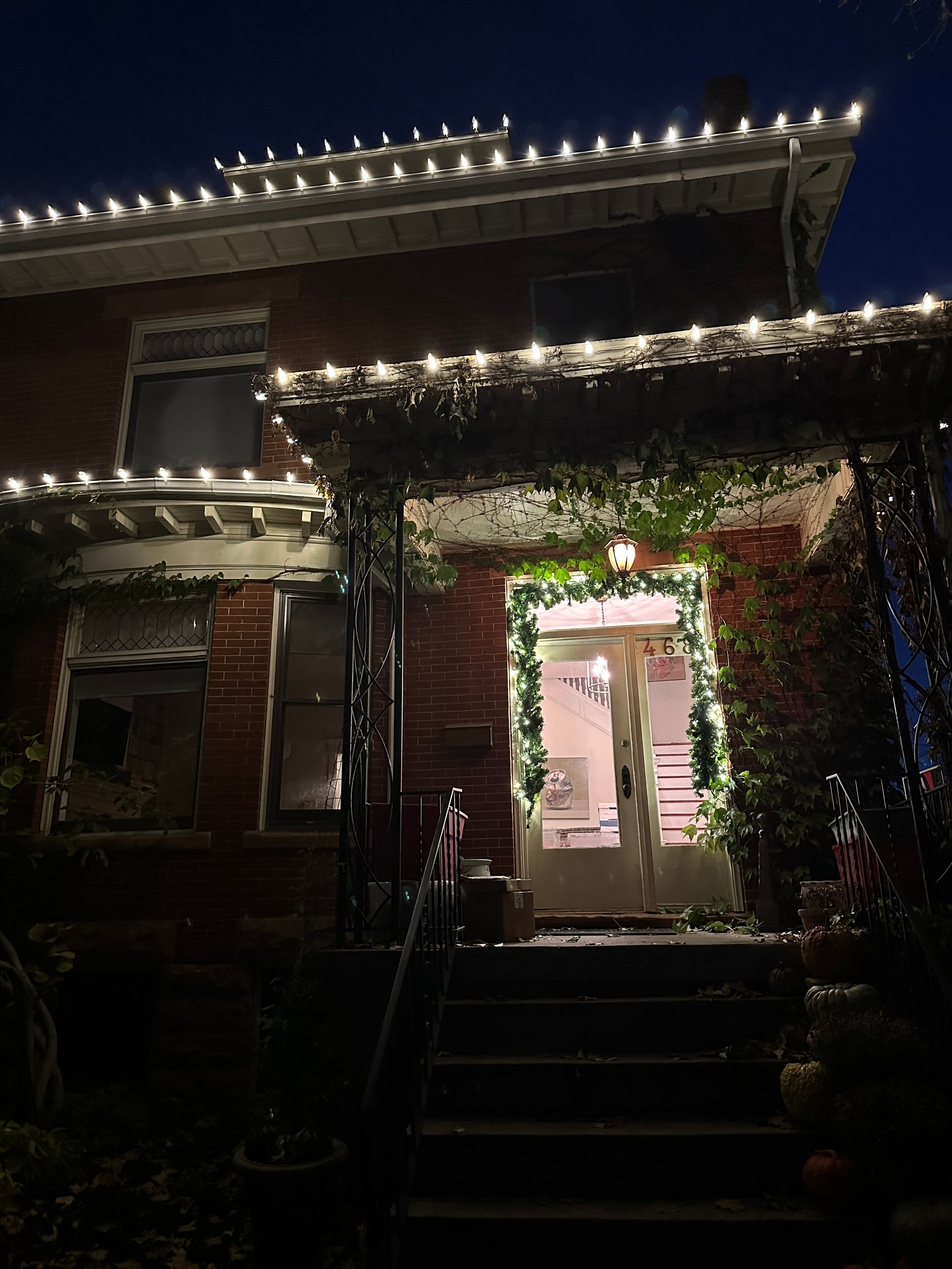 Brick house at night, decorated with white Christmas lights along the roofline and doorway.