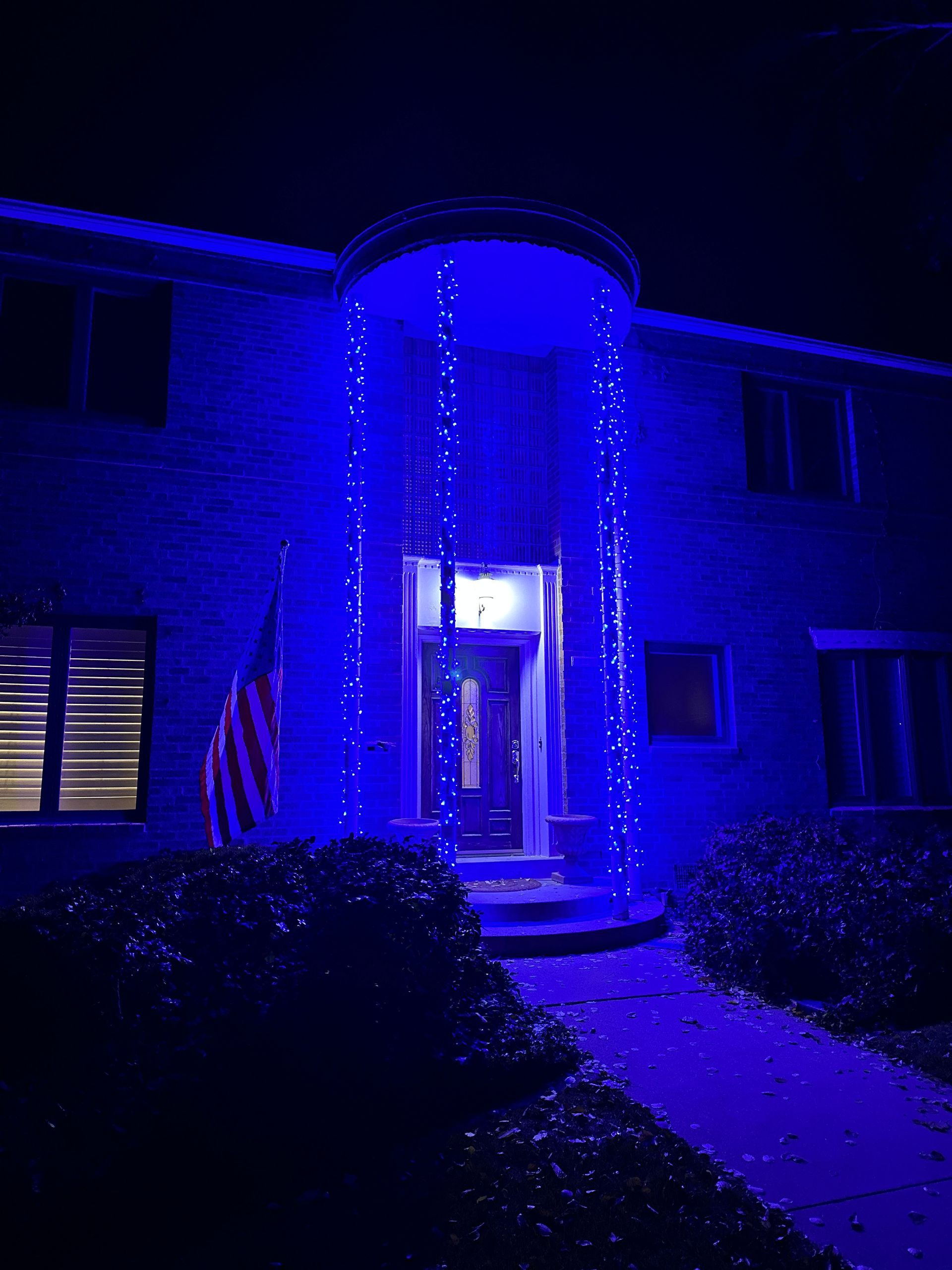 House lit with blue lights, American flag, at night.