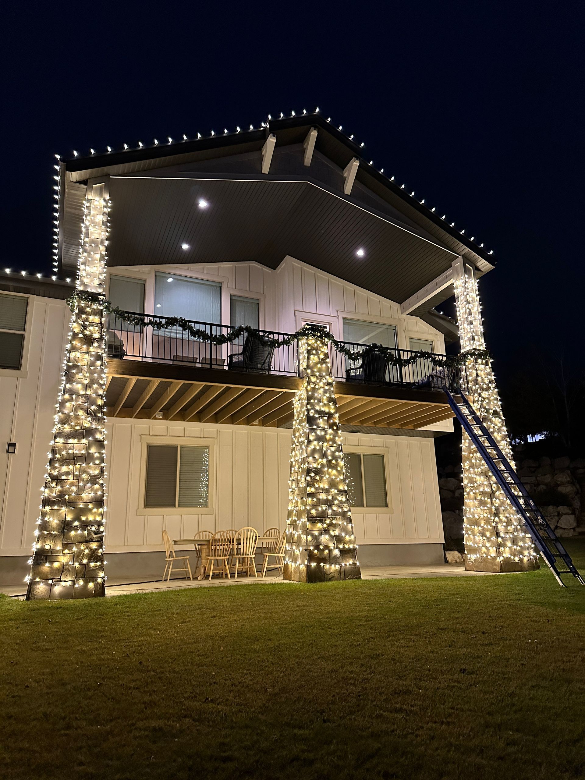 House decorated with white Christmas lights; columns, roofline, and balcony are illuminated. Night setting.