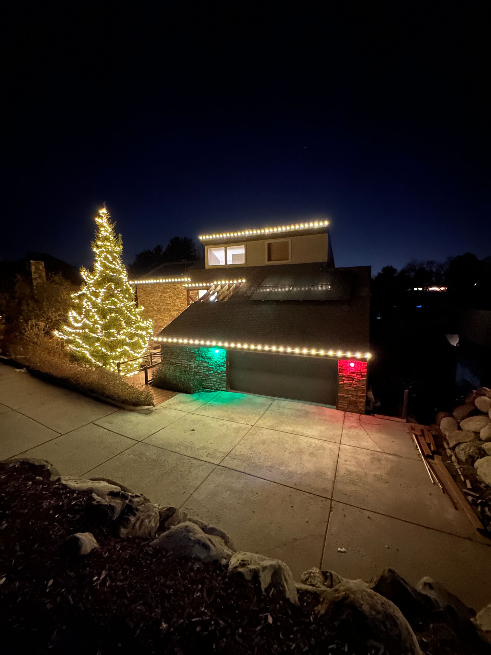 A house at night with Christmas lights. A lit Christmas tree and lights around the roof and garage.