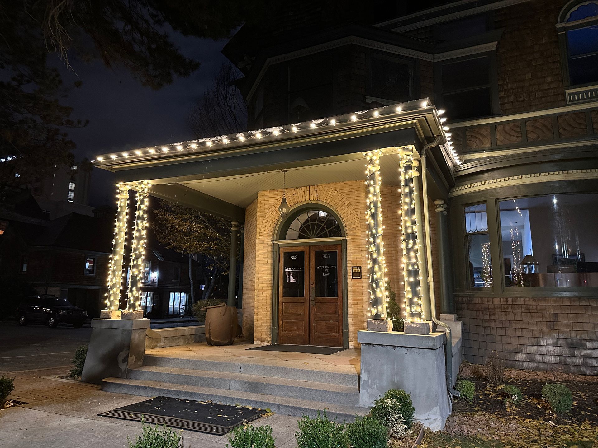 Entrance of a building with holiday lights at night. Brick, dark wood doors, and stone pillars.